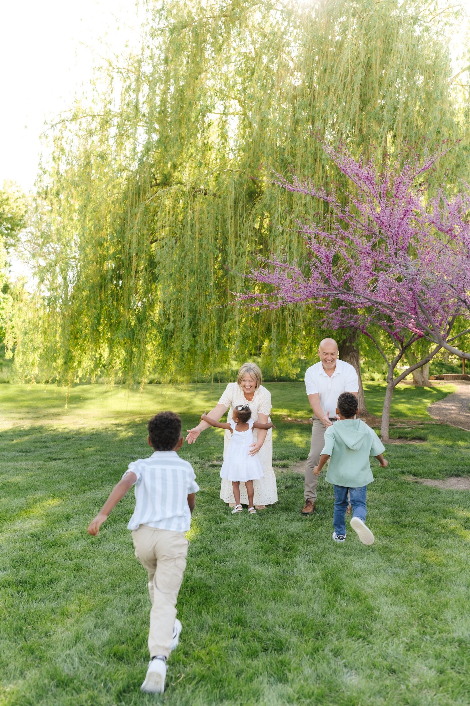 Family playing together on green lawn with blooming trees and weeping willows in background.