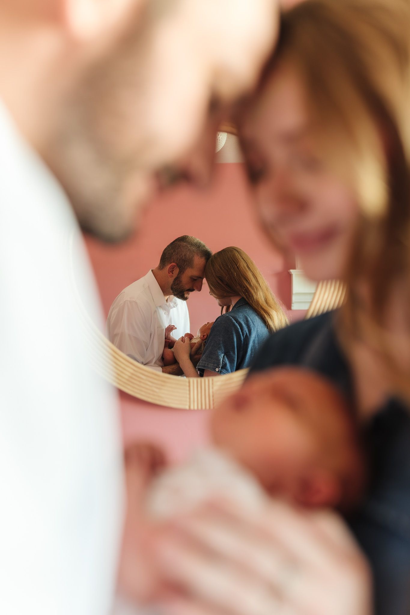 Parents tenderly holding newborn baby reflected in mirror, captured in intimate family portrait.