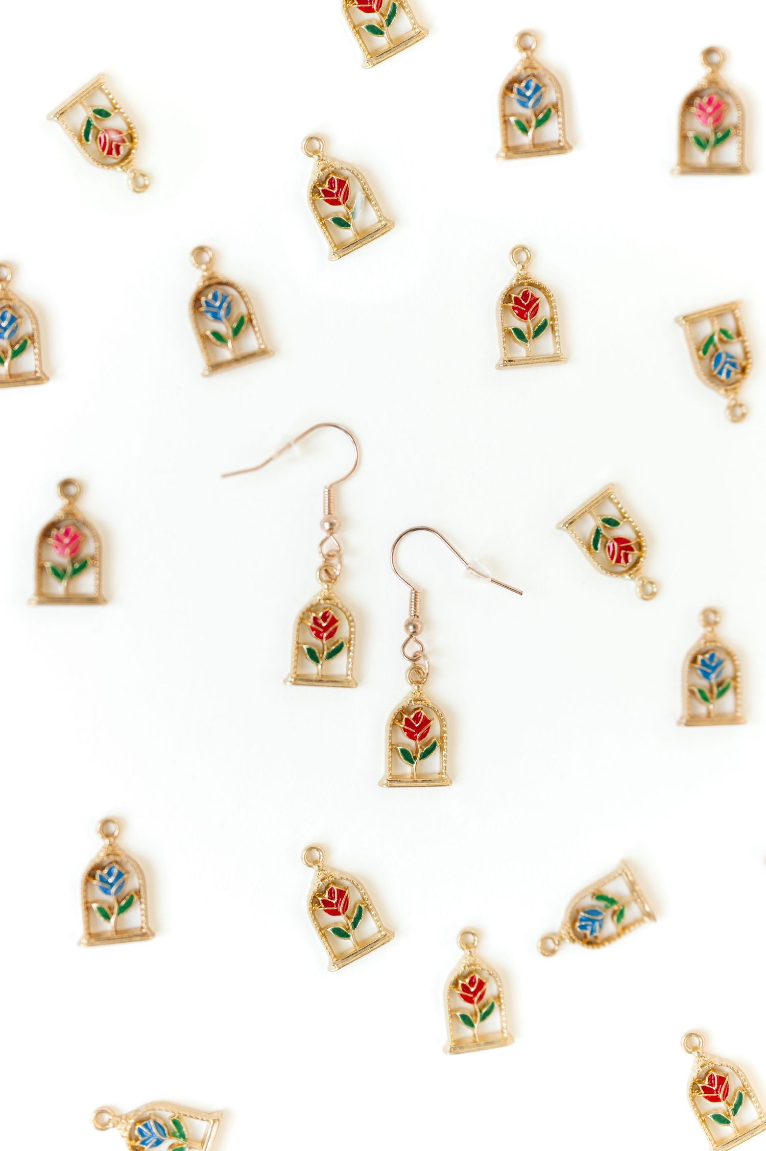 Pattern of small floral painted earrings arranged on white background.