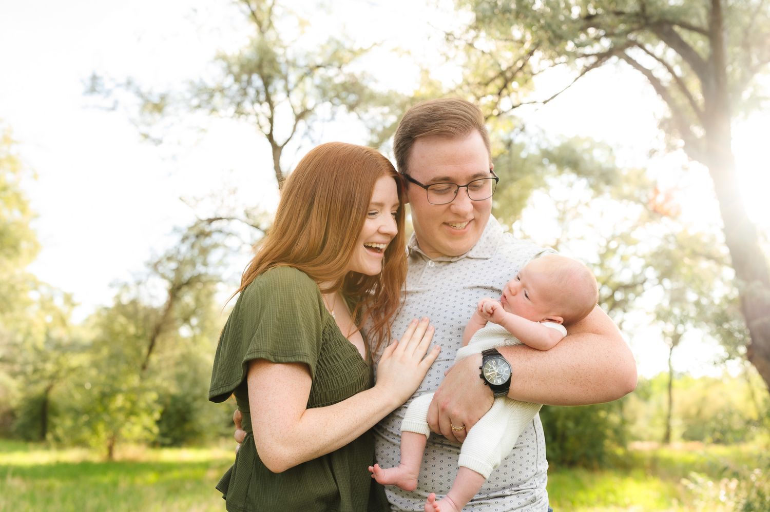 Family embracing in golden sunlight among trees wearing casual spring attire.