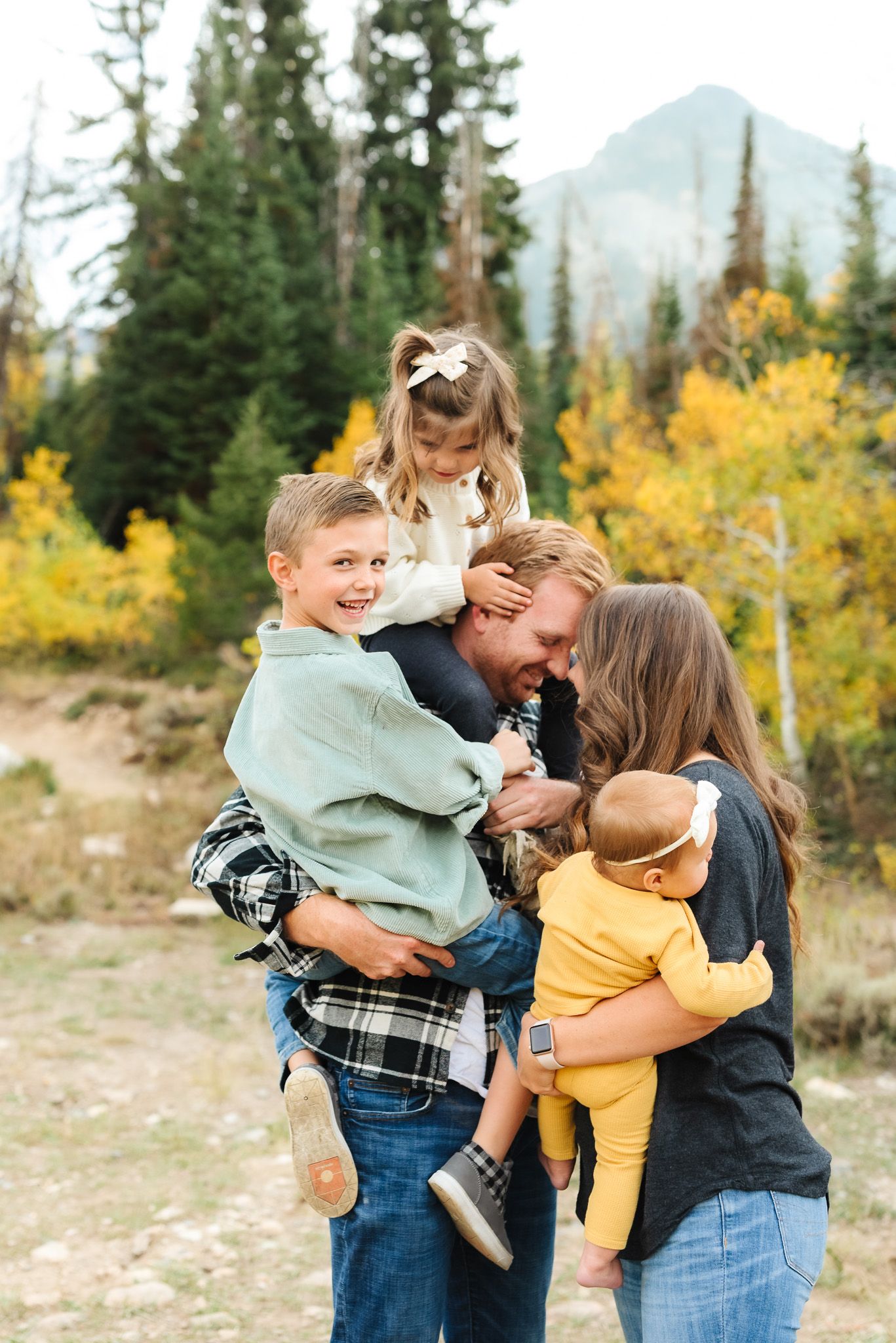 Family embraces and laughs together during fall photo session in mountain setting.