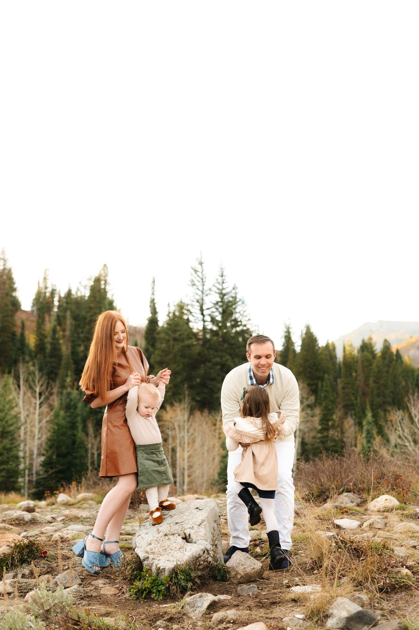 Family enjoying a playful moment together in a mountain setting with evergreen trees and rocks.