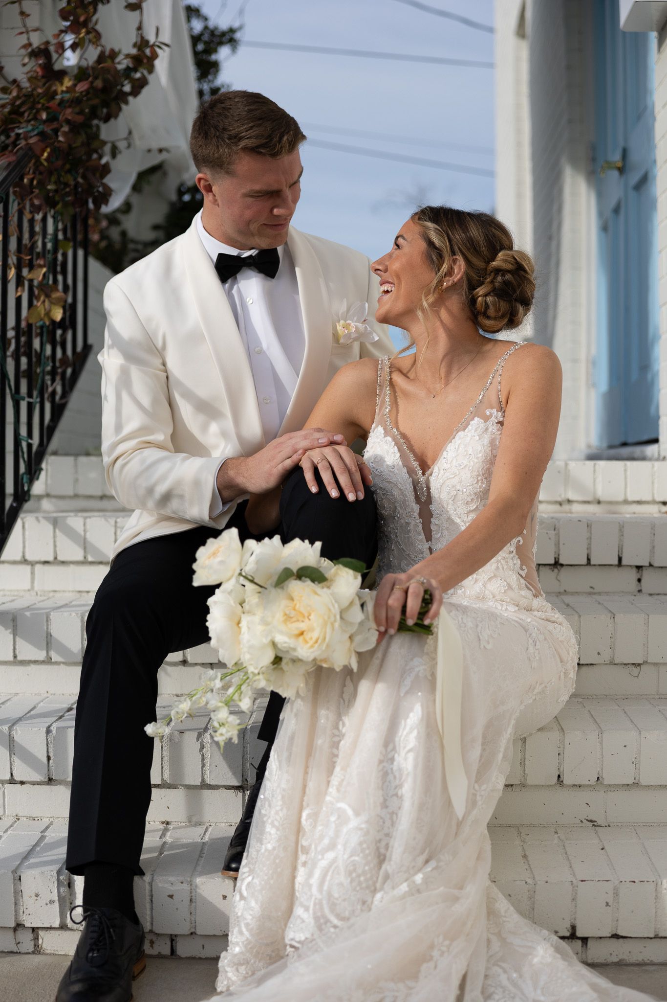 Newlyweds in formal attire share joyful moment on white brick porch.