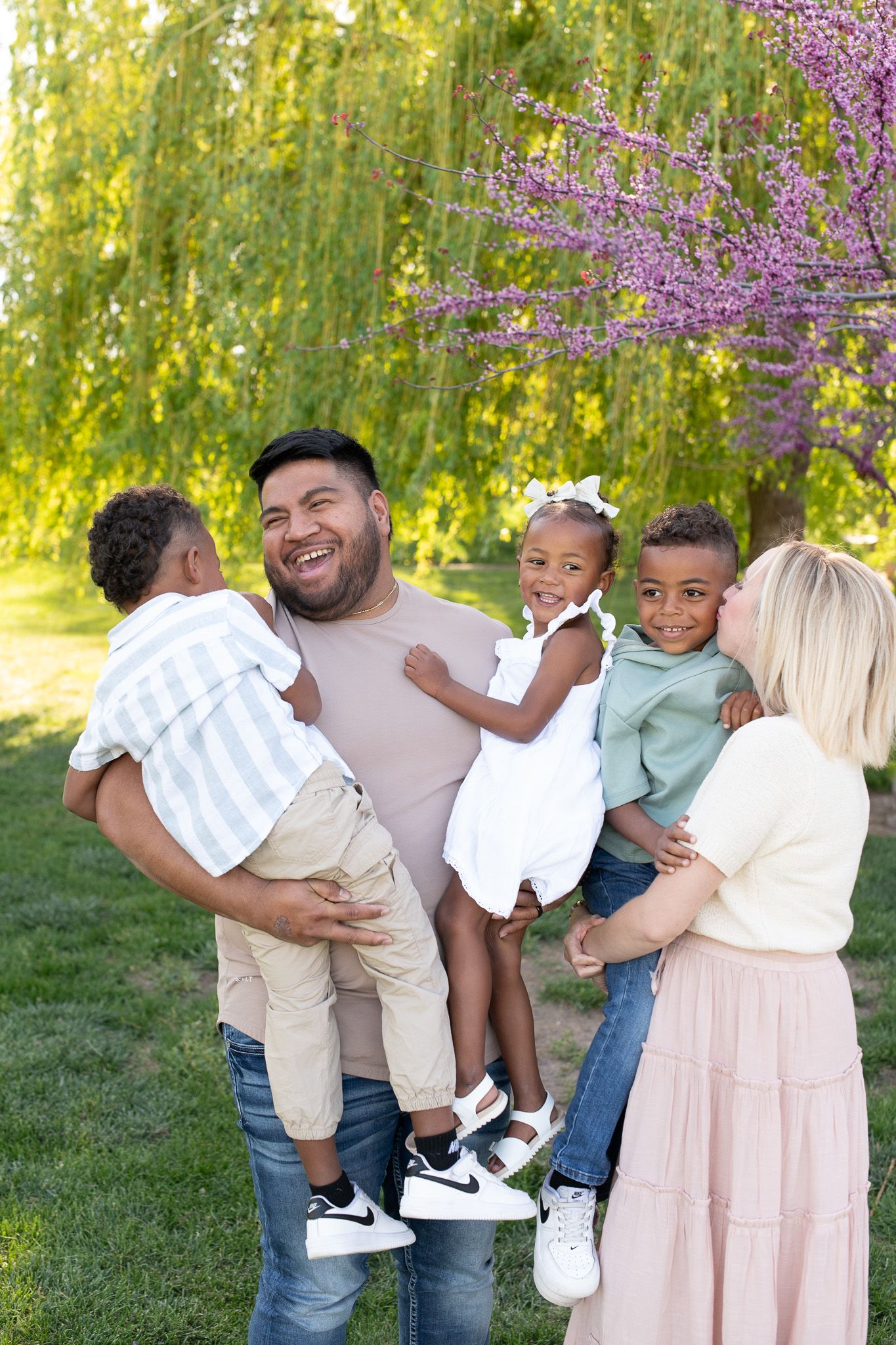 Happy multiracial family with three young children enjoying a sunny day outdoors near blooming trees in a park.
