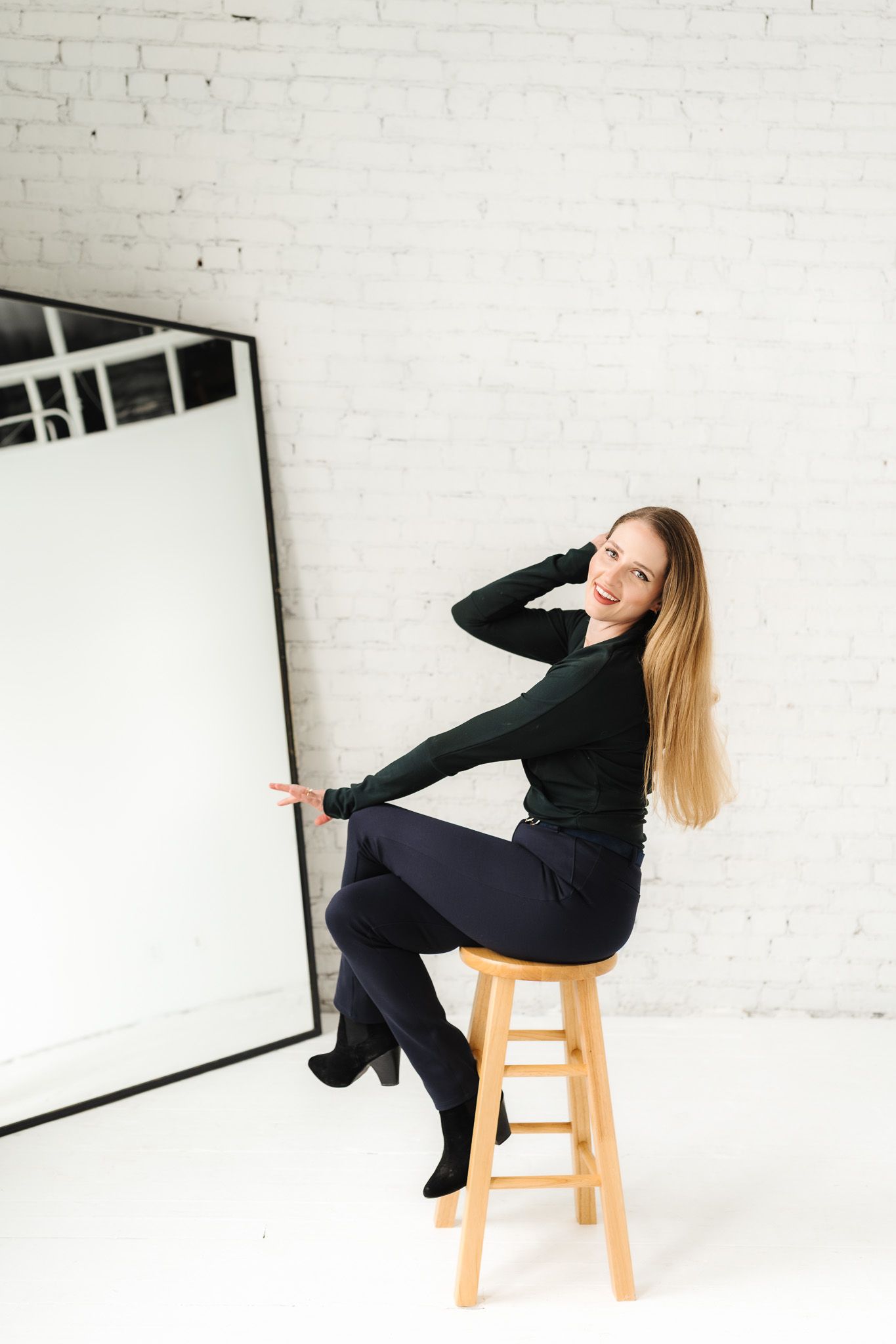 Minimalist studio photoshoot featuring poses on wooden stool against white brick wall.
