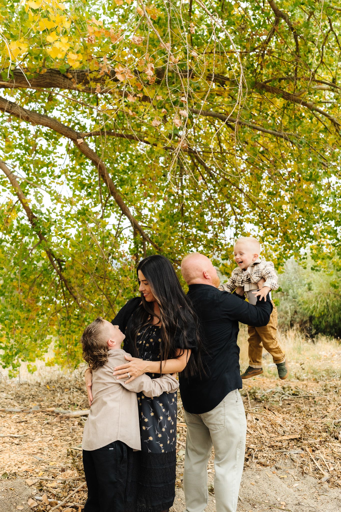 Family embracing and sharing joyful moments under trees with autumn leaves.