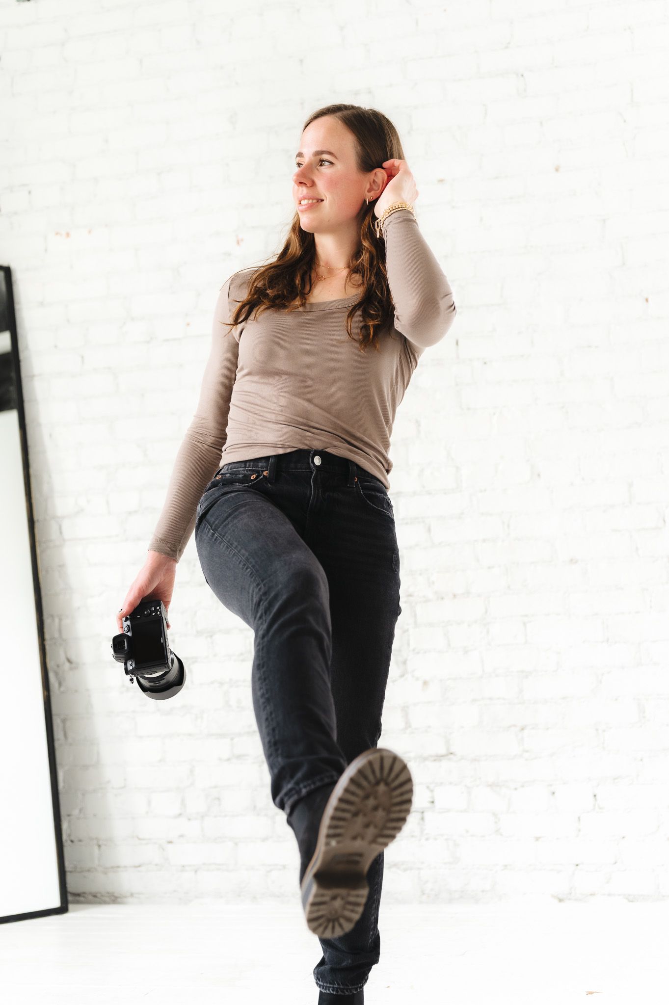 Dynamic studio pose showing movement while holding camera equipment against white wall.