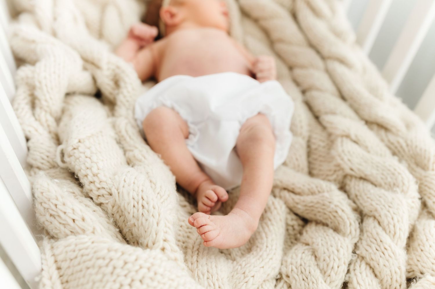 Newborn baby rests peacefully on textured cream cable knit blanket during photo shoot.