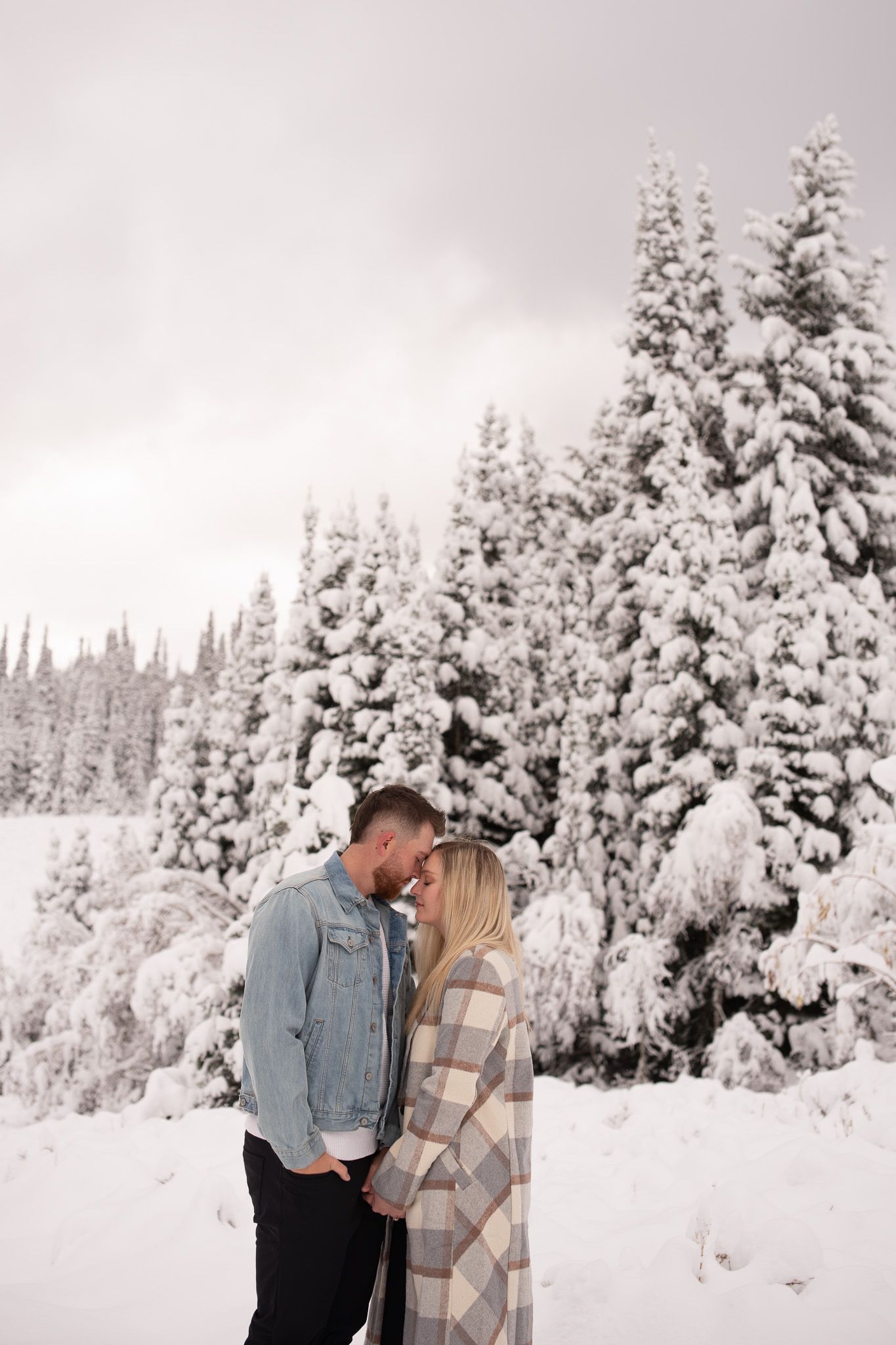 Couple sharing a romantic moment in a snowy winter landscape with snow-covered pine trees.
