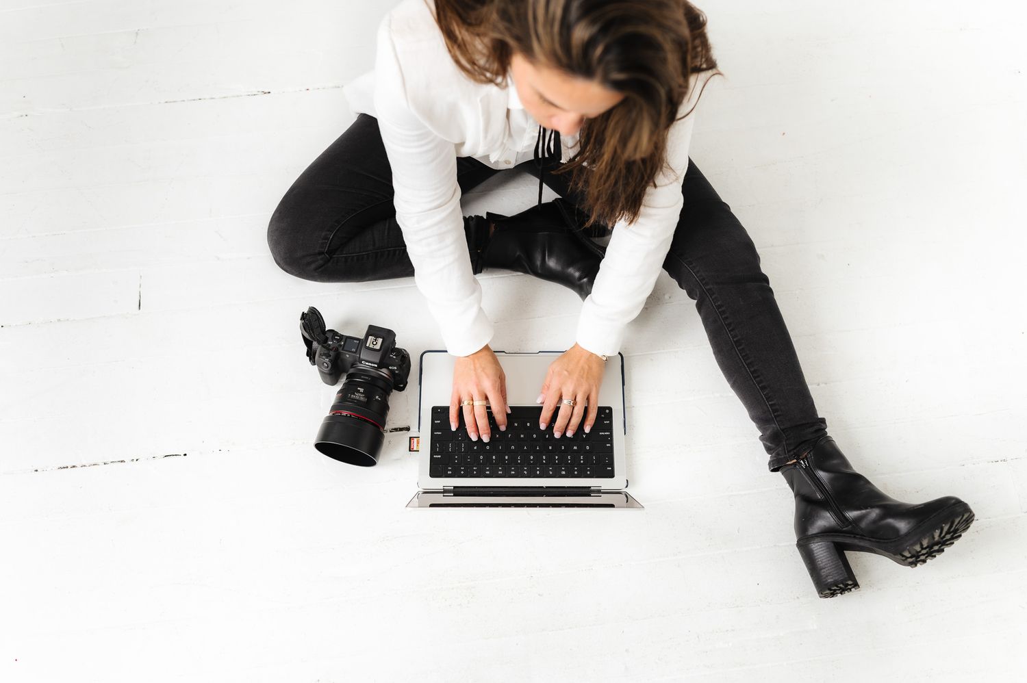 Overhead view of photographer working on laptop with camera beside on white floor.
