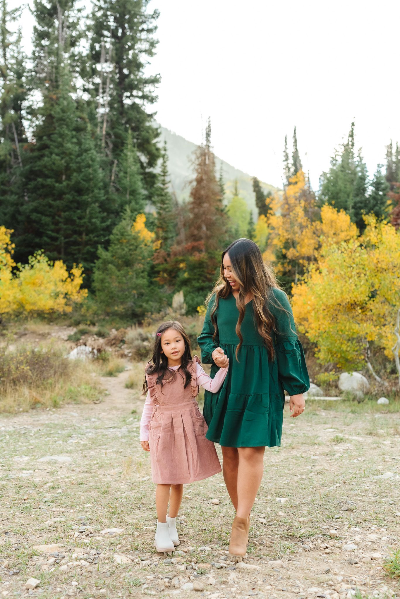 Family members walk together on a mountain trail surrounded by vibrant yellow fall foliage and evergreen trees.
