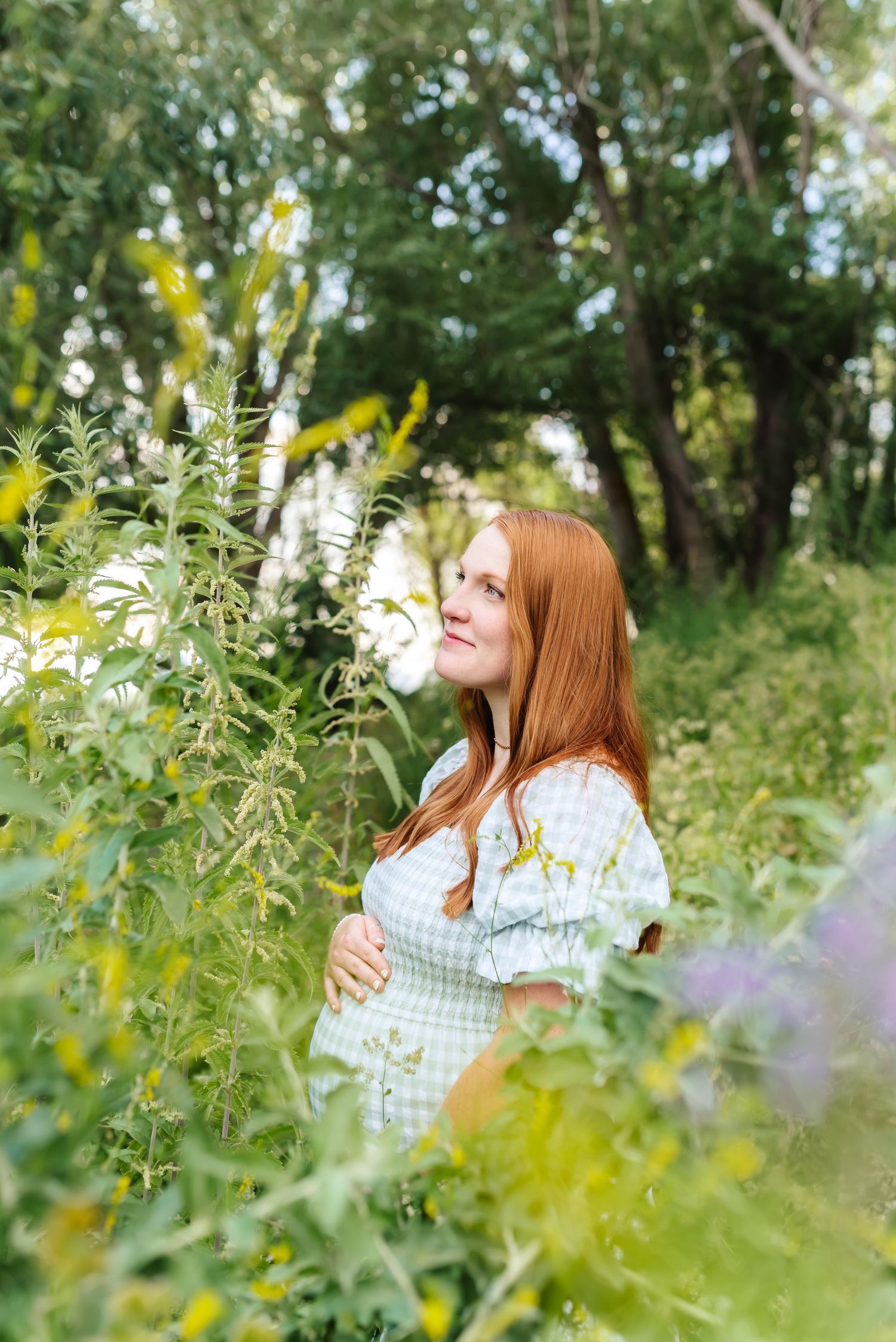 Woman in gingham dress poses among wildflowers and greenery in natural setting.