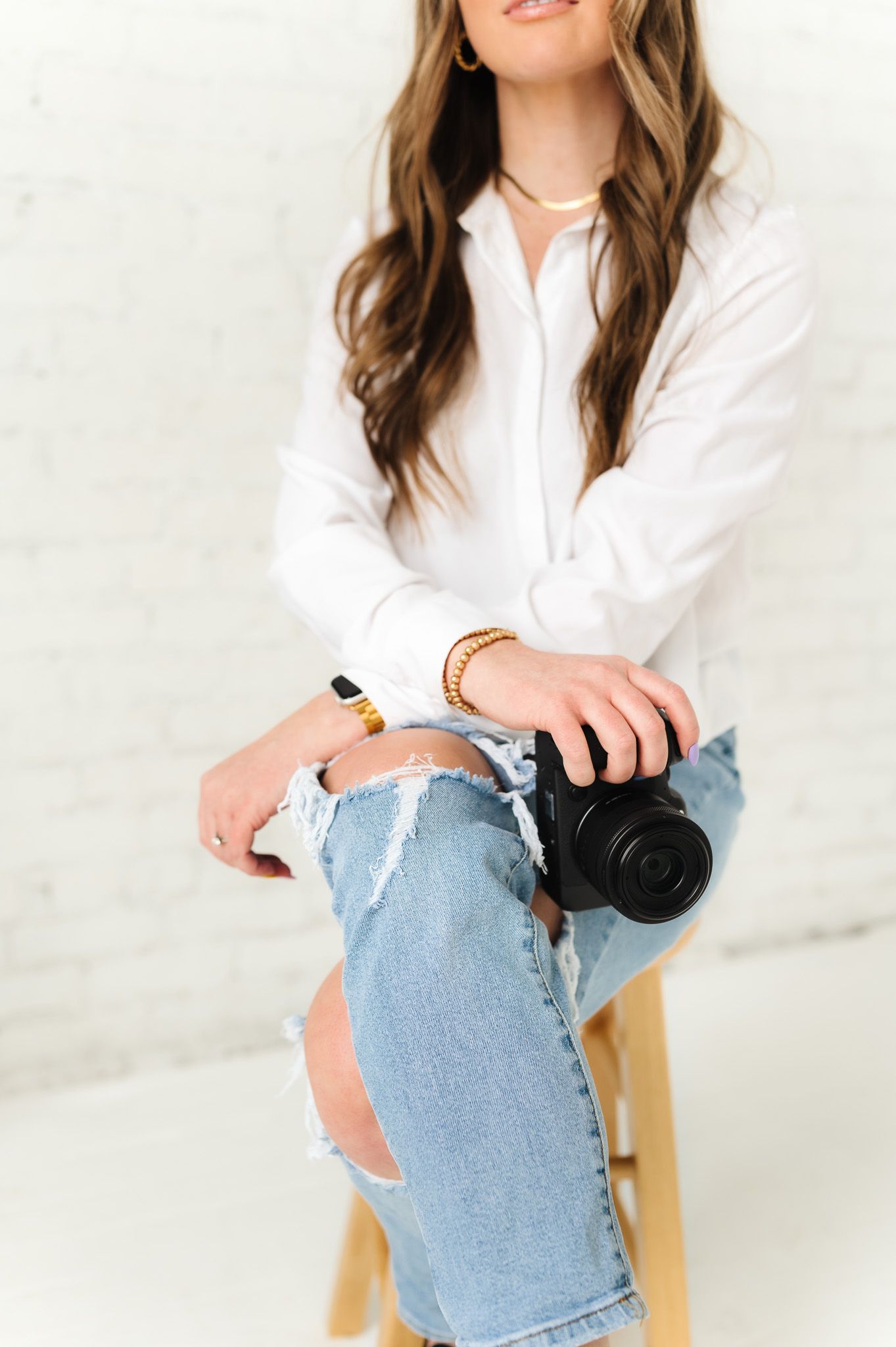 Detail shot of photographer with camera wearing white button-down and distressed jeans.