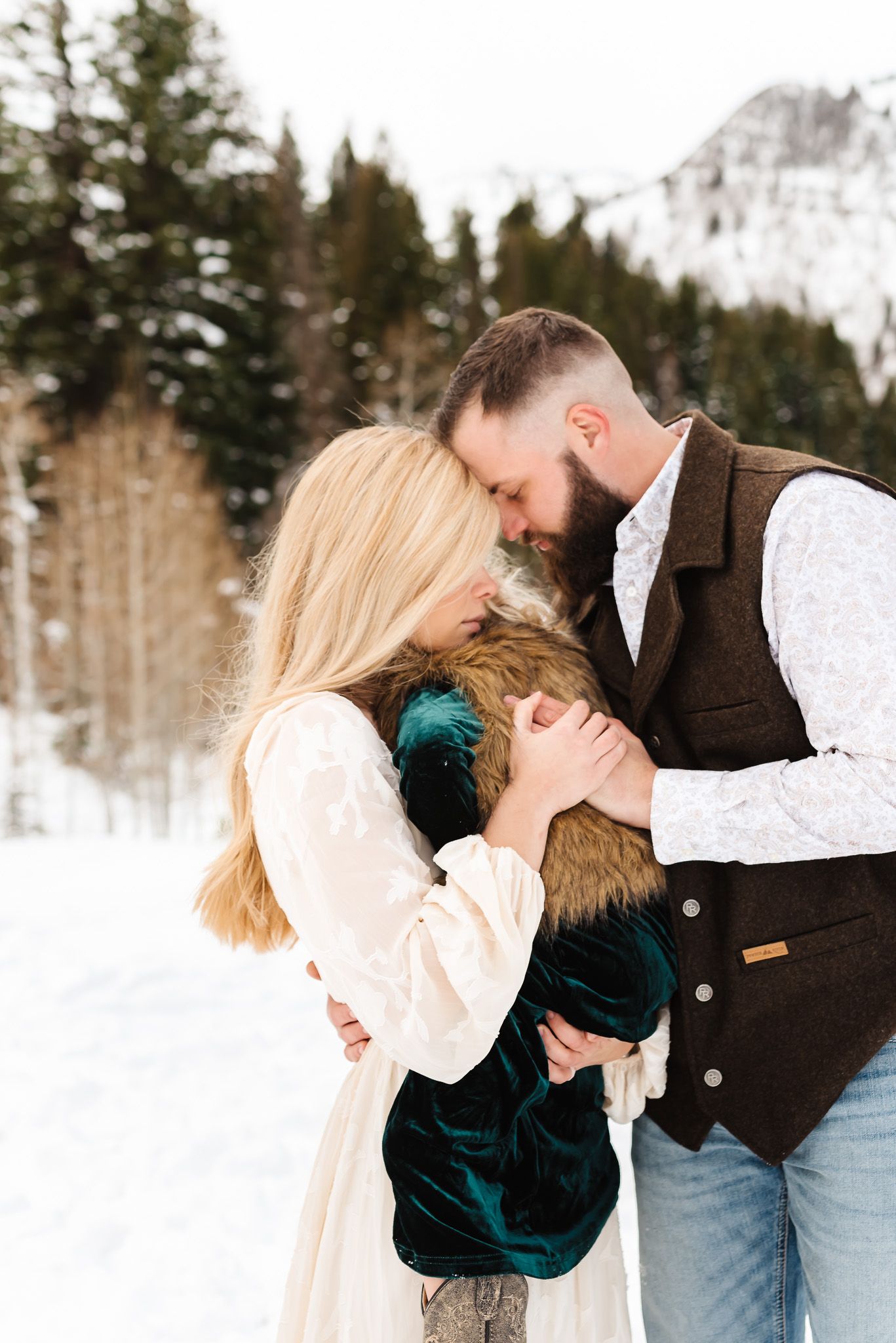 Couple shares intimate winter moments in a snowy forest wearing coordinating cream and brown outfits.