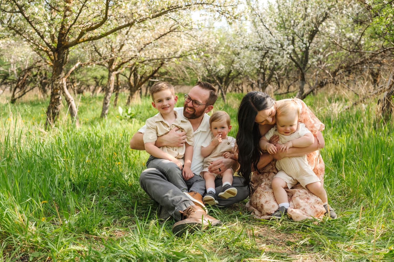 A family sits together on green grass in a natural outdoor setting during a spring day.