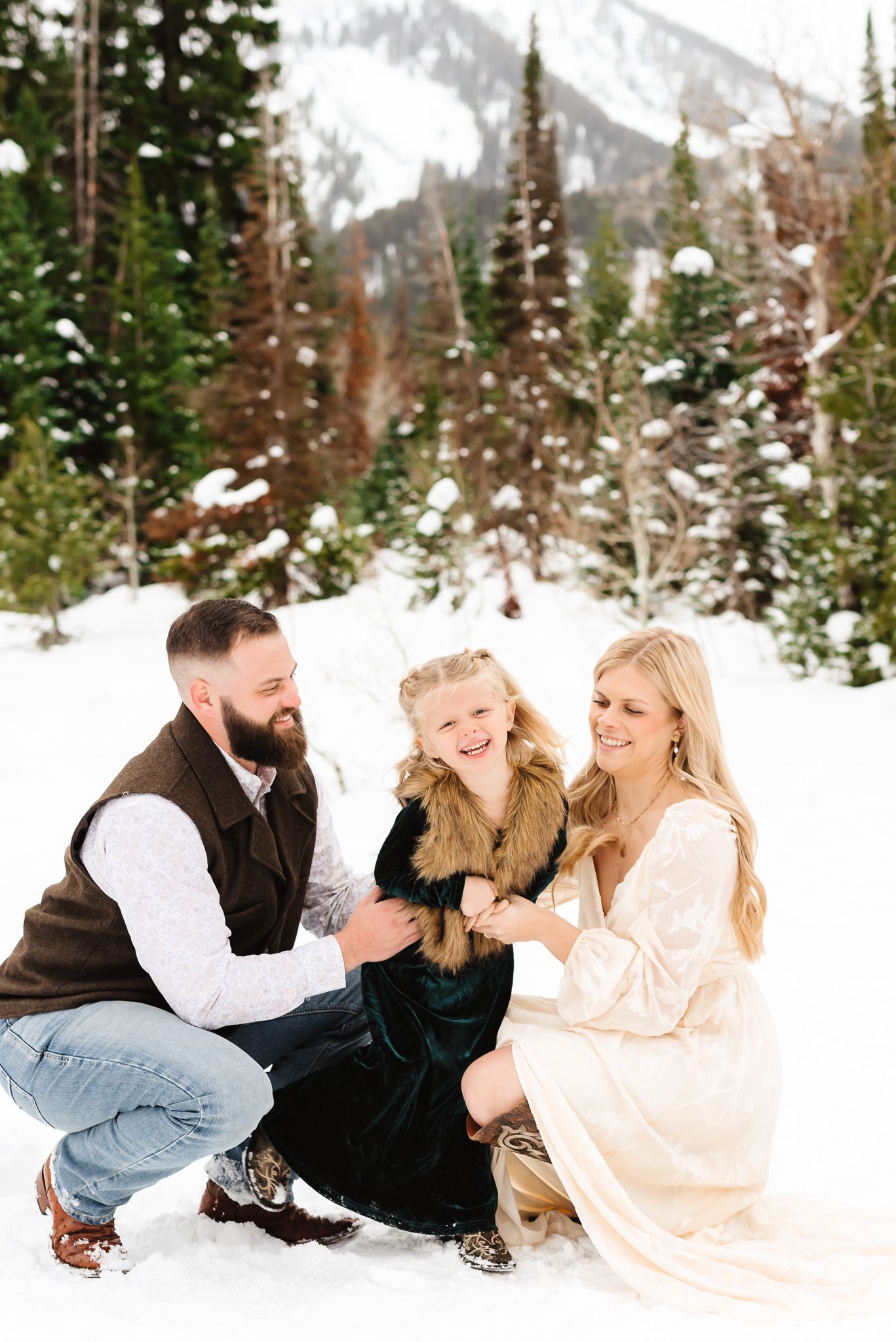Family enjoying a playful moment together while sitting in the snow with mountain scenery behind them at Jordan Pines in Big Cottonwood