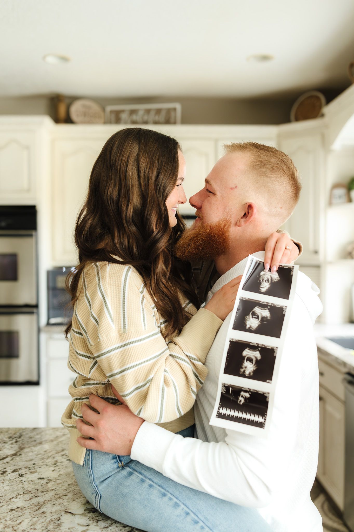 Tender embrace shared between couple with ultrasound photos in bright kitchen.
