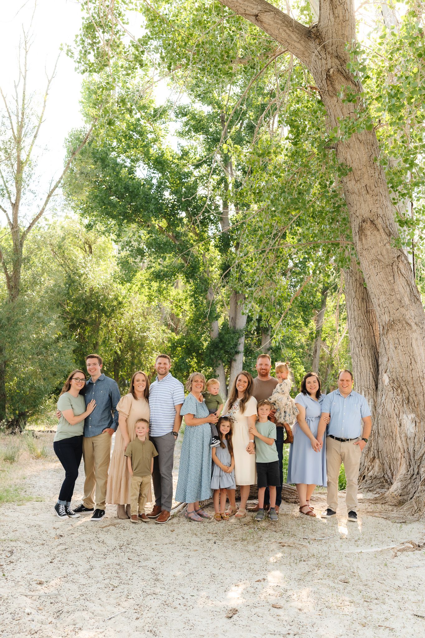 Family group photo session under mature trees with natural lighting and casual poses.