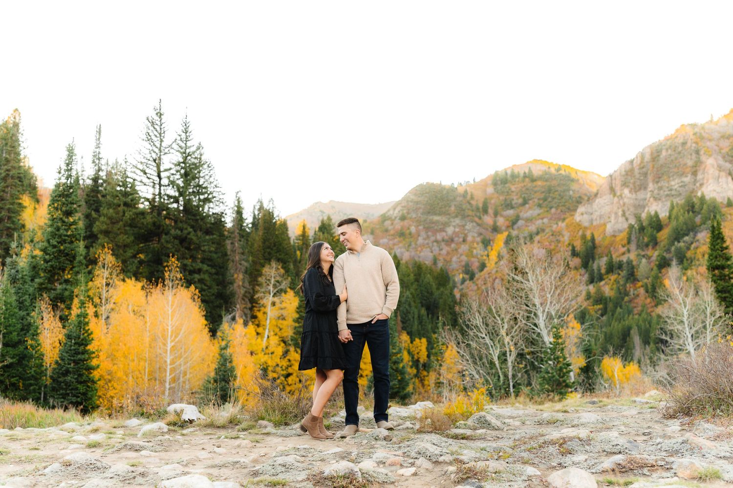 A person stands alone on a mountainside surrounded by autumn colored trees.