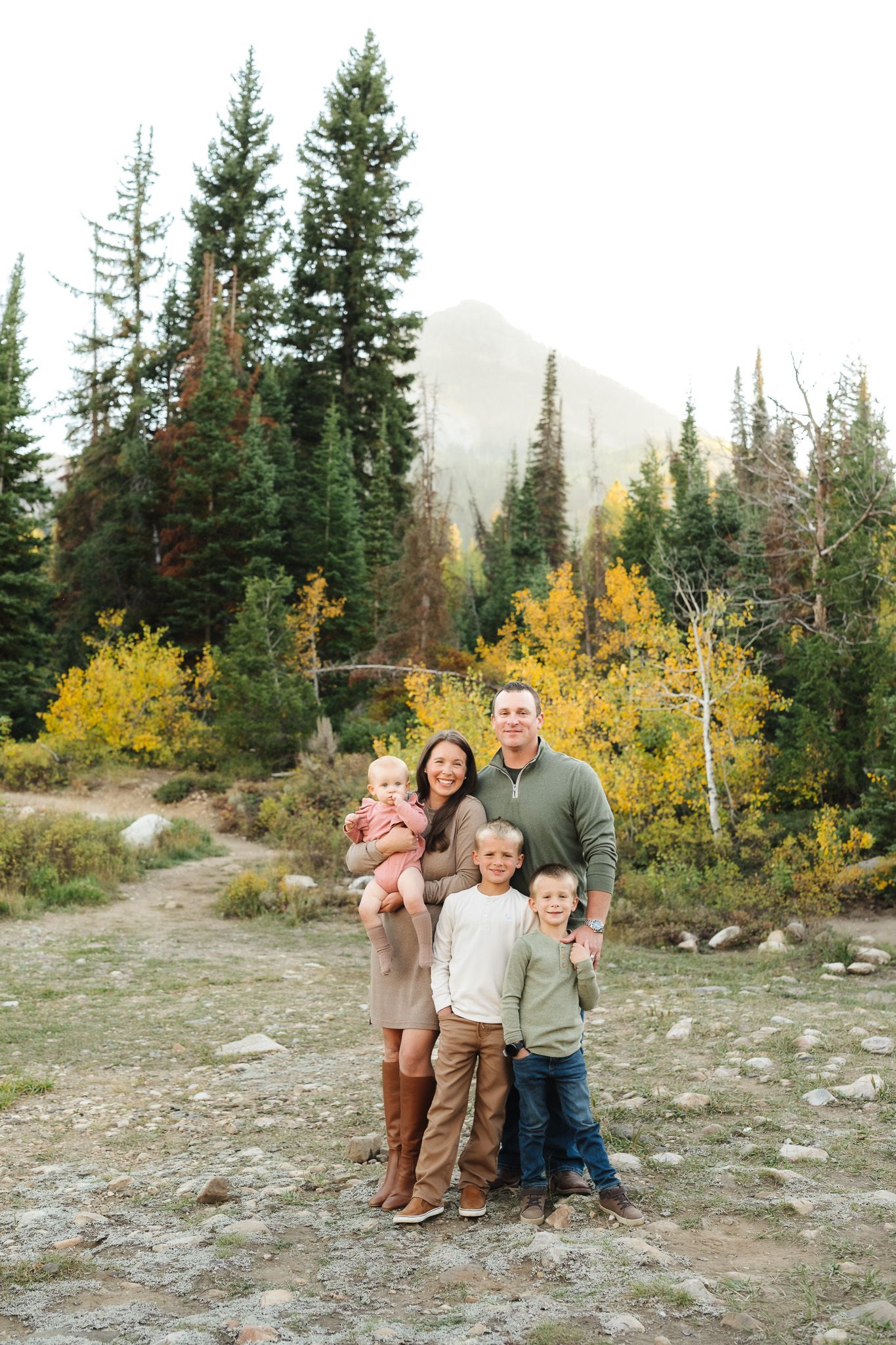 Playful family jumping and dancing together in a mountain clearing with fall colors.