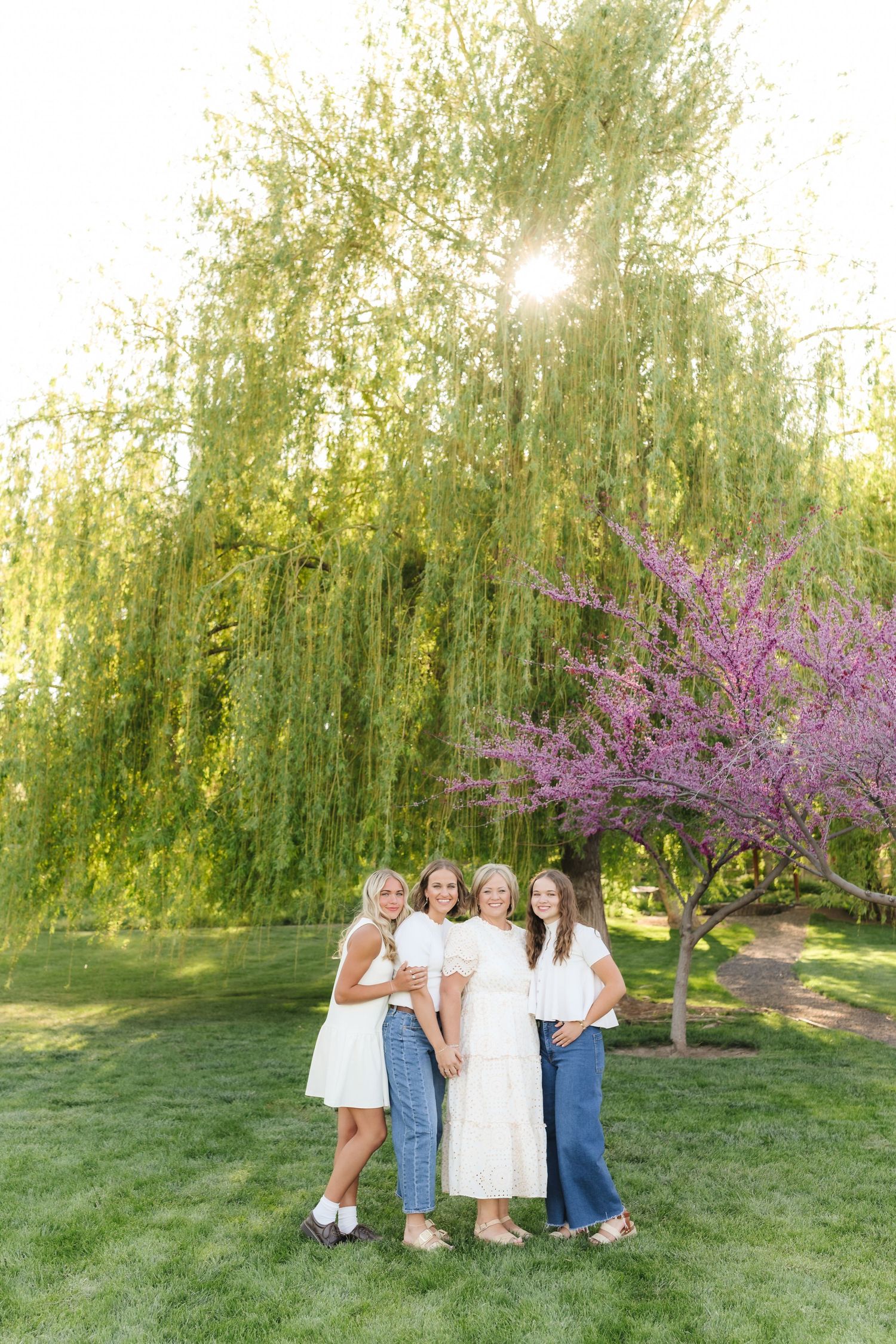 Group poses together in front of blooming pink cherry blossom trees and weeping willows on a grassy lawn.