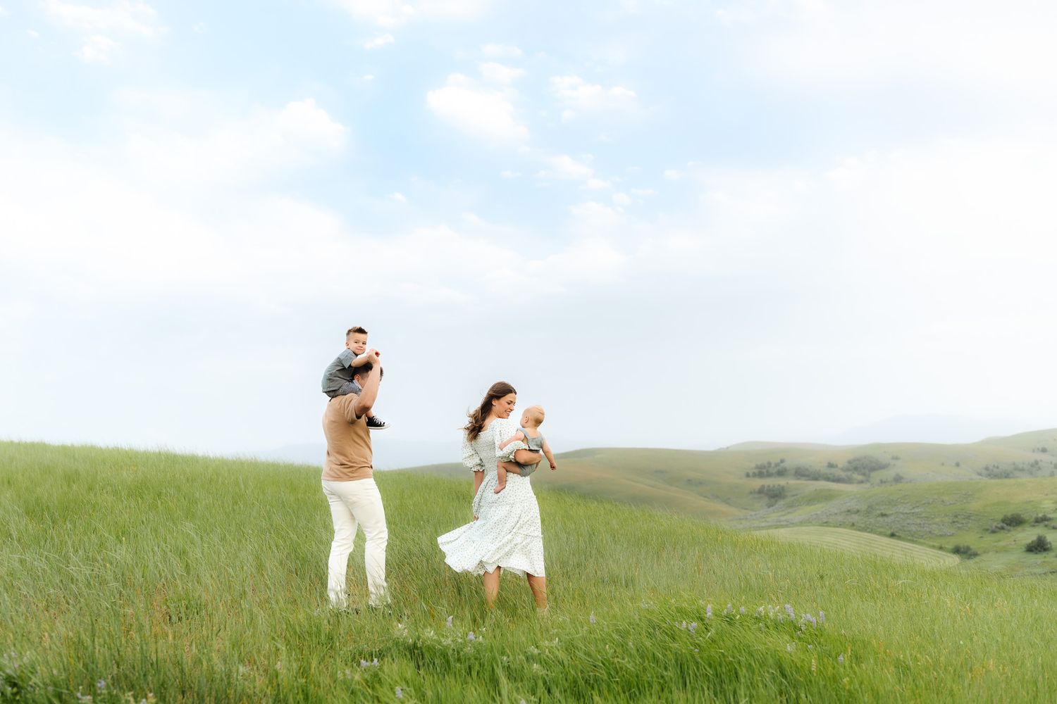 Romantic photoshoot in vast green meadow with distant mountains and blue sky.