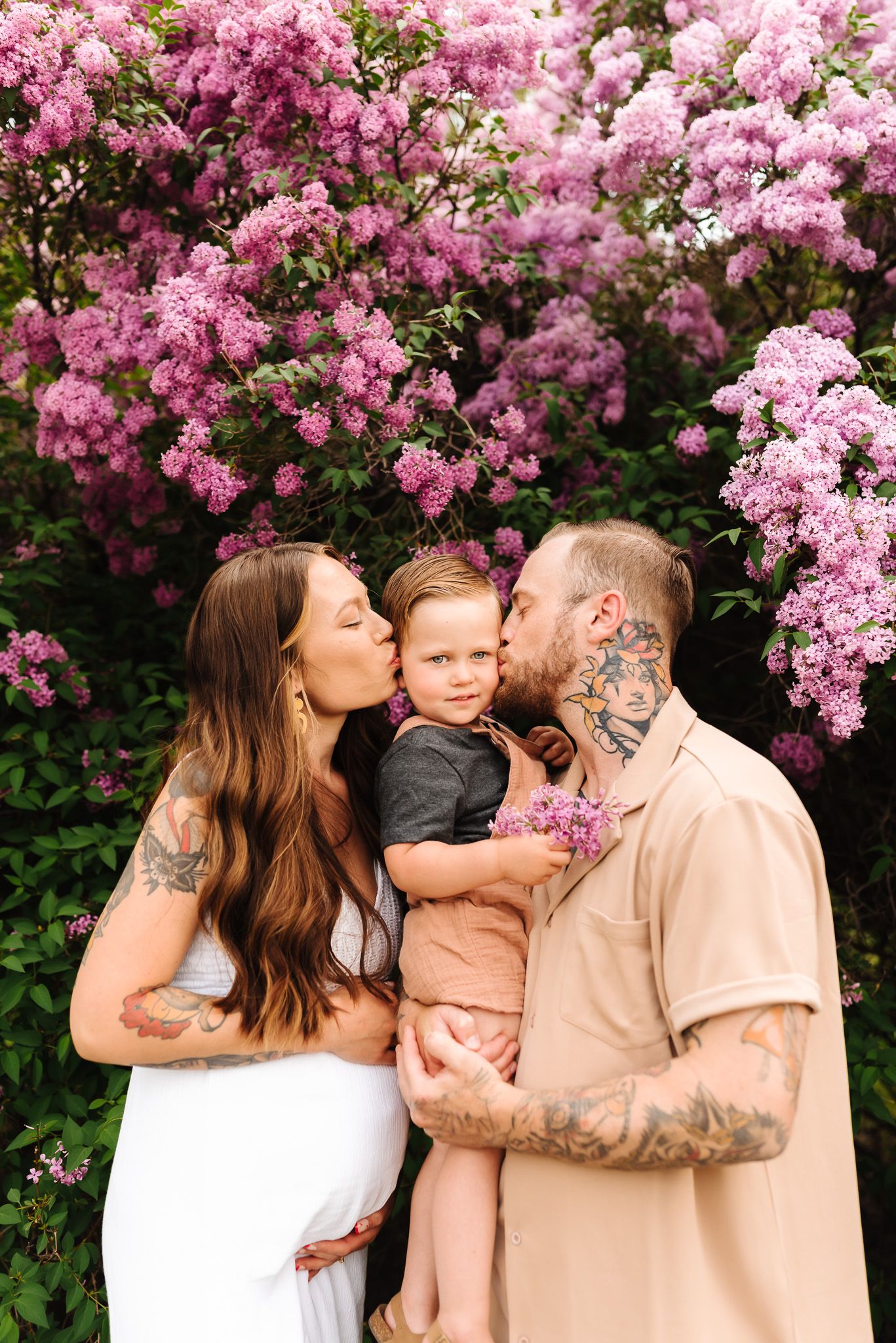 Intimate family moment captured in front of blooming pink crepe myrtle bush.
