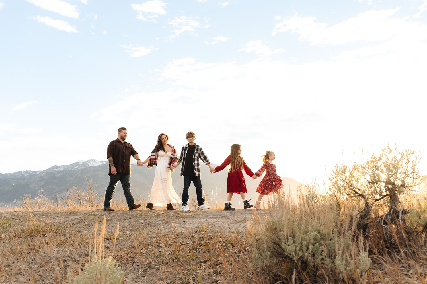 A group of people walk along a scenic mountain ridge at sunset creating silhouettes against the golden sky.