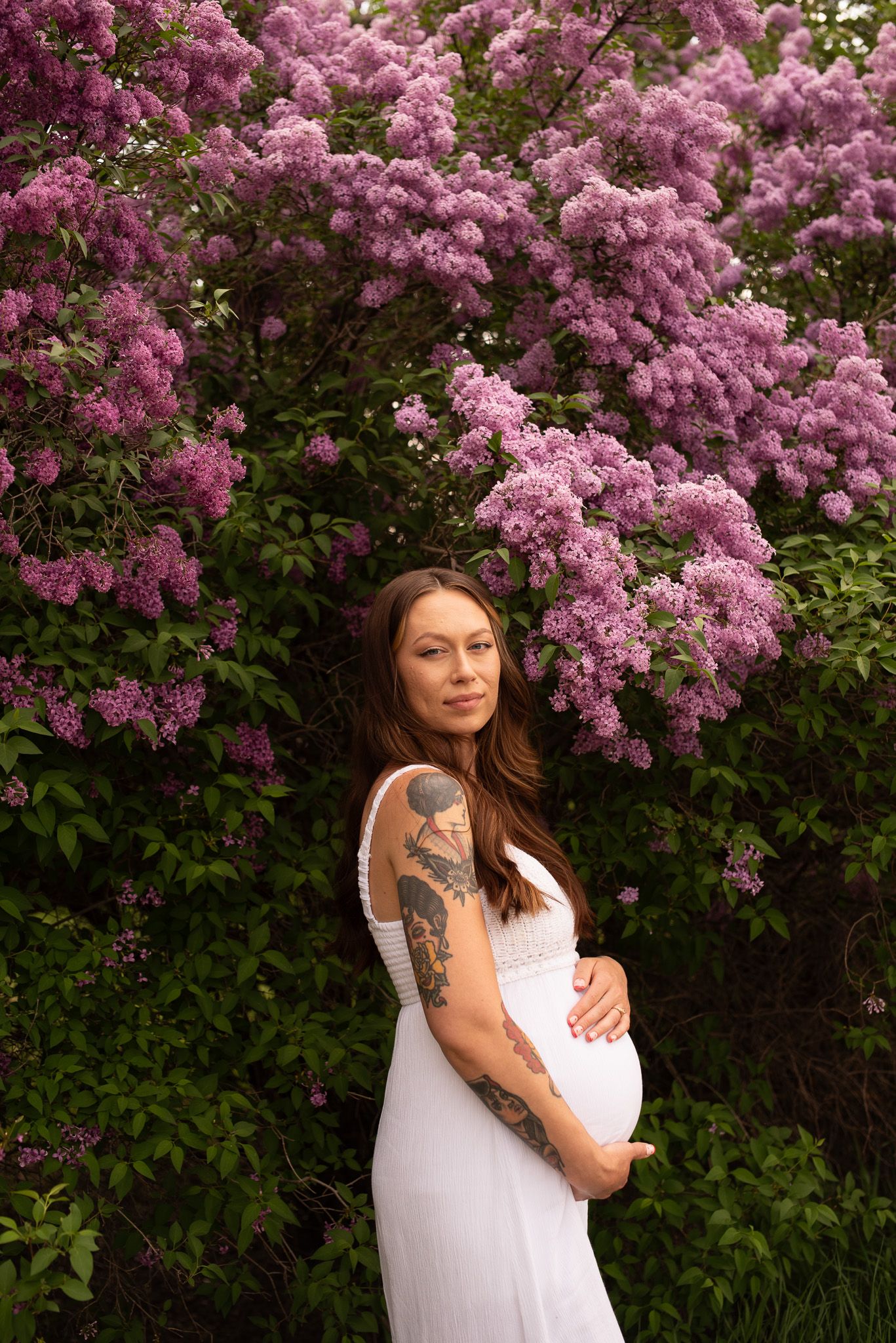 Maternity portrait against blooming lilac bush showcases spring beauty.
