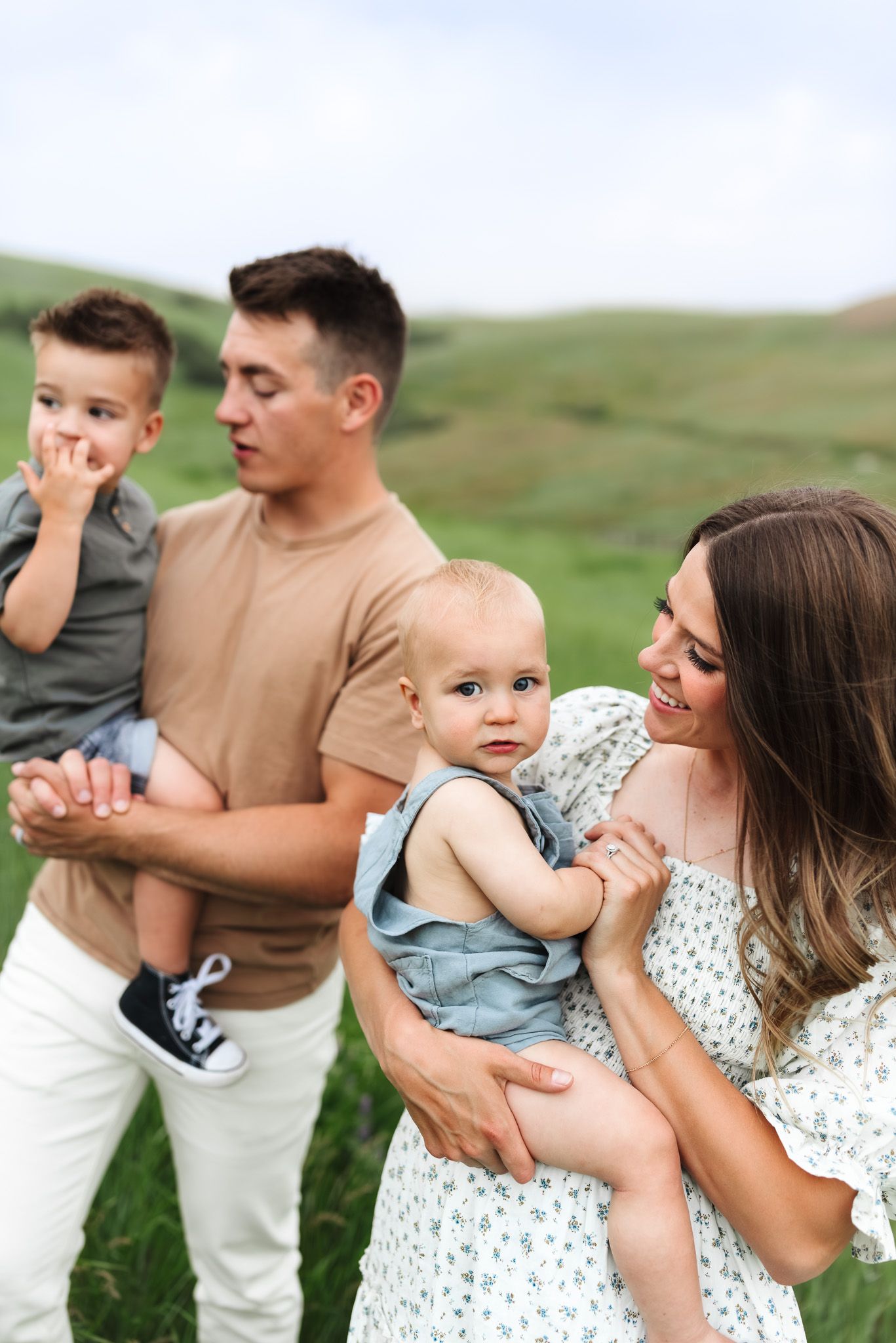 Happy young family with two children enjoying outdoor time in a green meadow on a cloudy day.