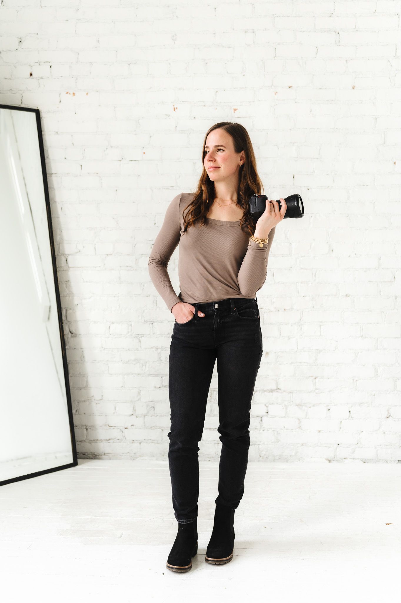 Photographer in casual attire poses with camera in bright studio setting.