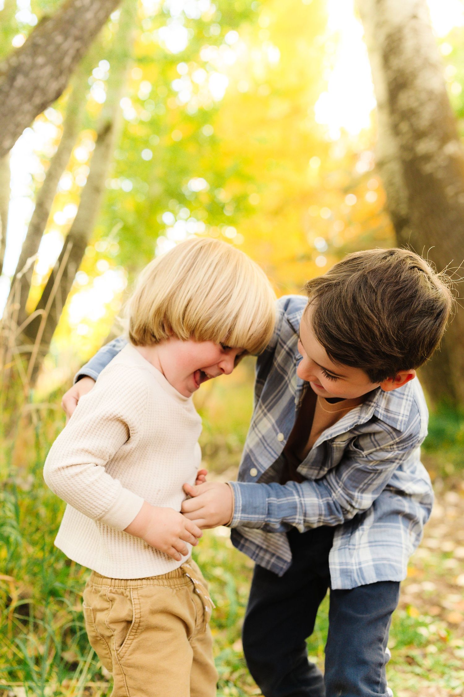 Playful interaction between family members in casual attire against a fall foliage backdrop.