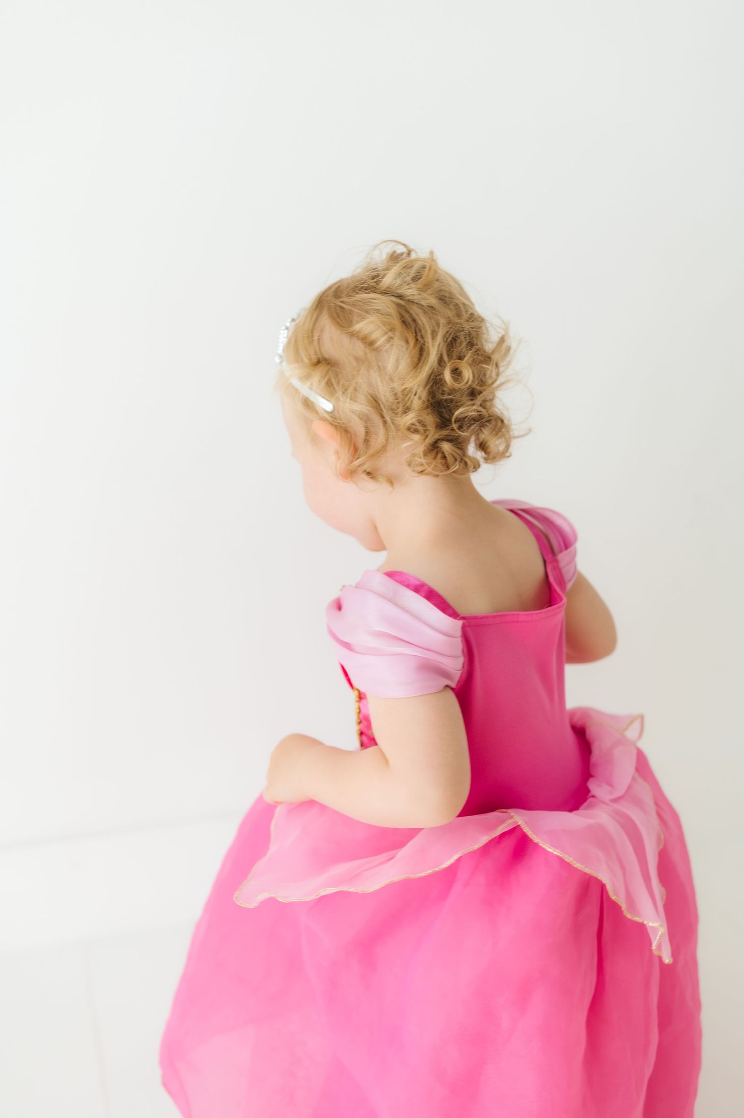 Back view of child wearing pink princess ball gown with curly blonde hair.