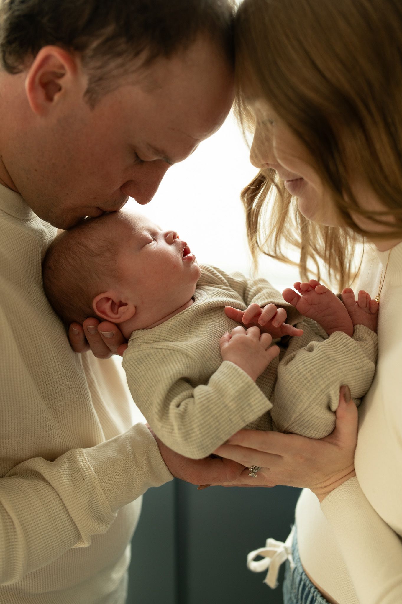 New parents lovingly cradle their newborn baby, with father kissing infant's head in a tender family portrait.