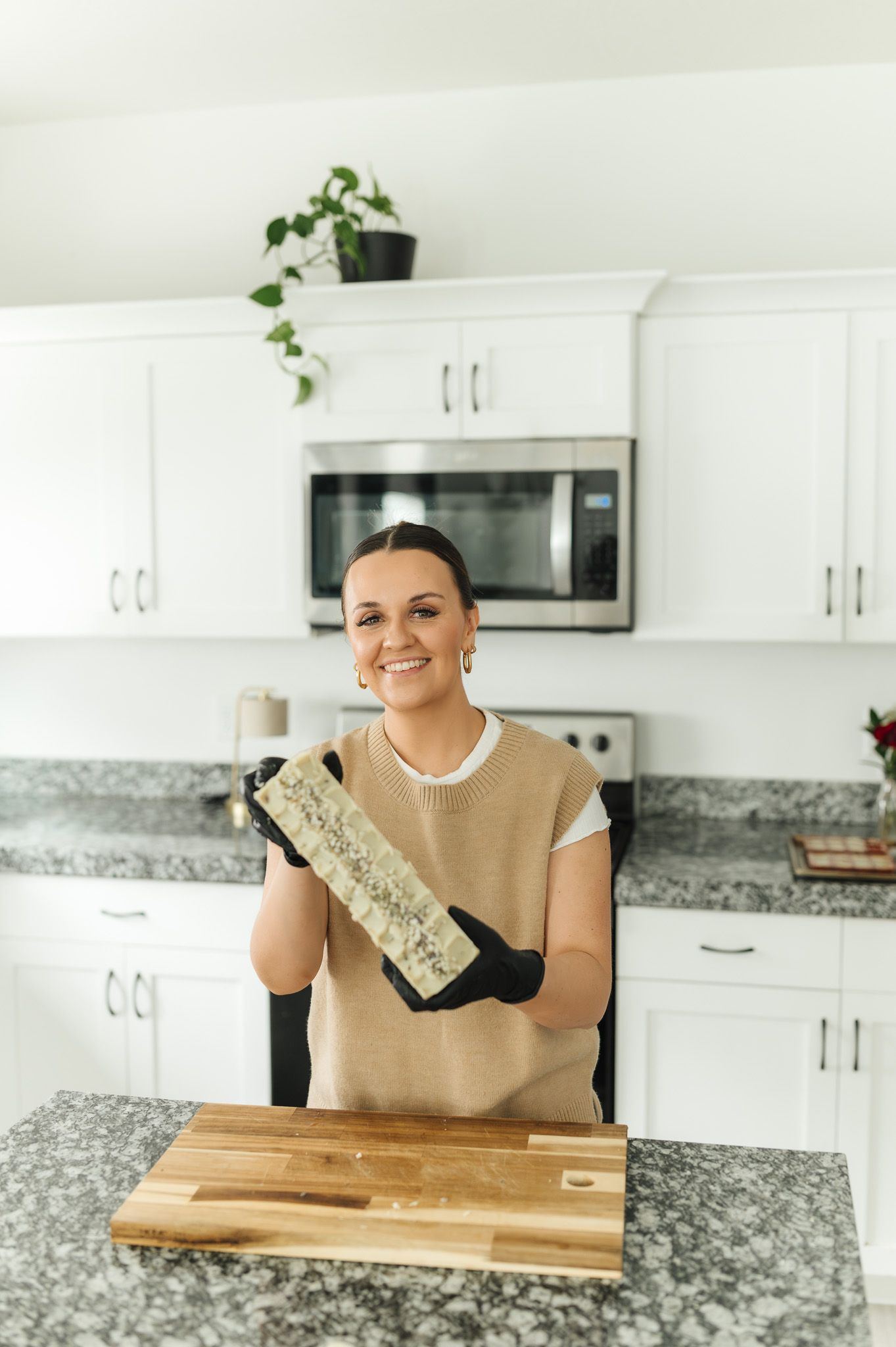 A person wearing black gloves prepares food on a wooden cutting board in a modern white kitchen with granite countertops.