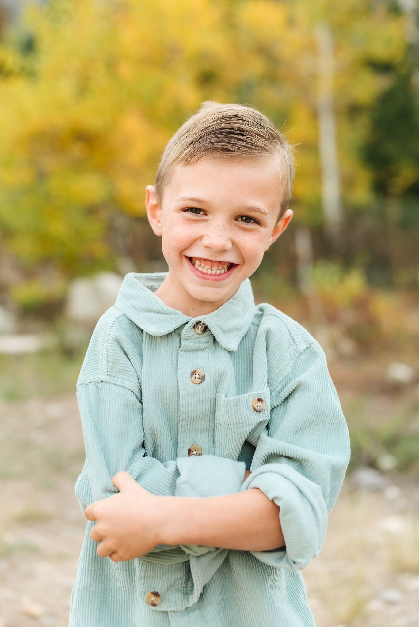 Child in mint green sweater poses playfully against autumn mountain backdrop.