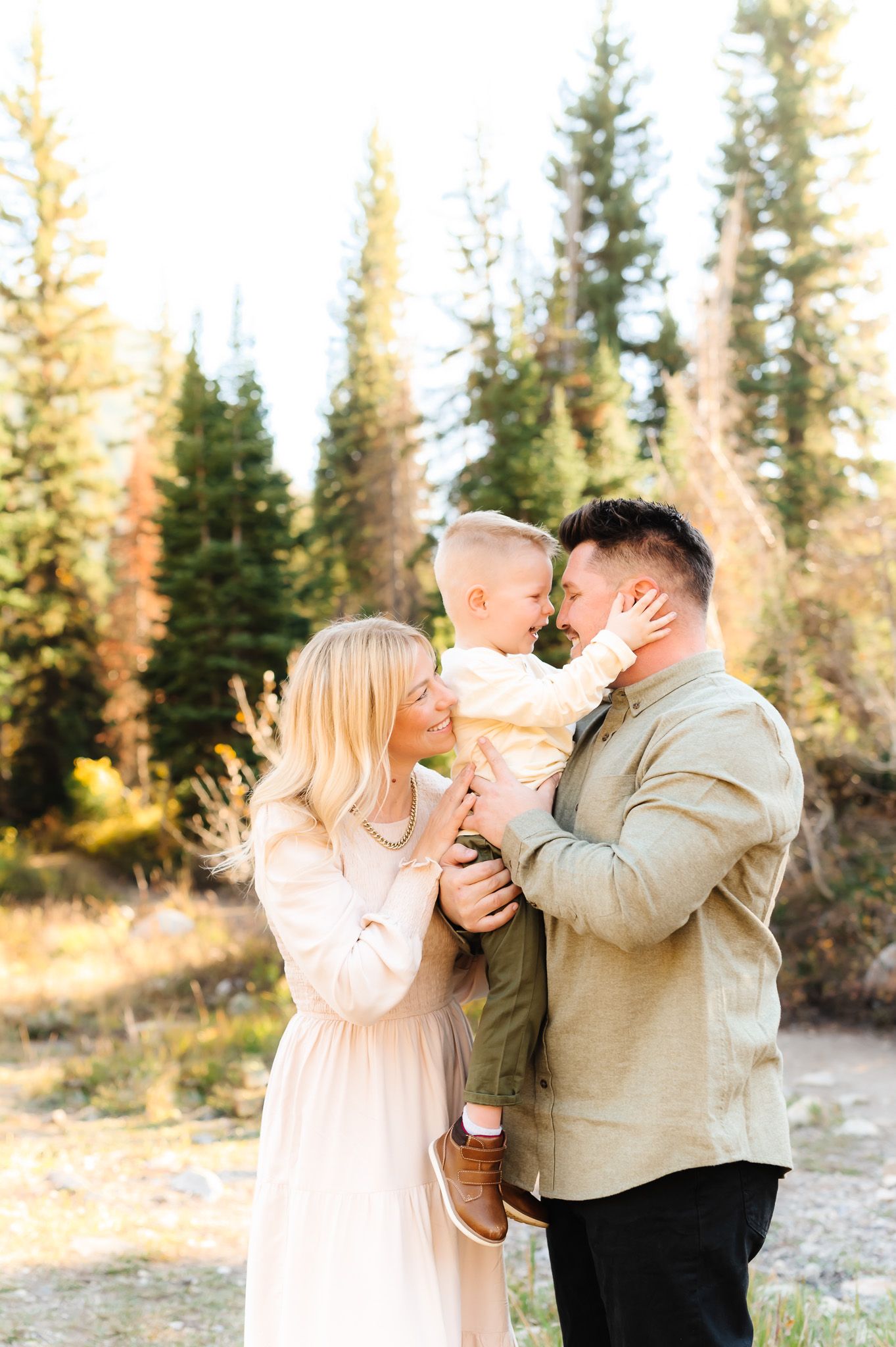 A sweet family moment captured in golden sunlight with evergreen trees in the background.