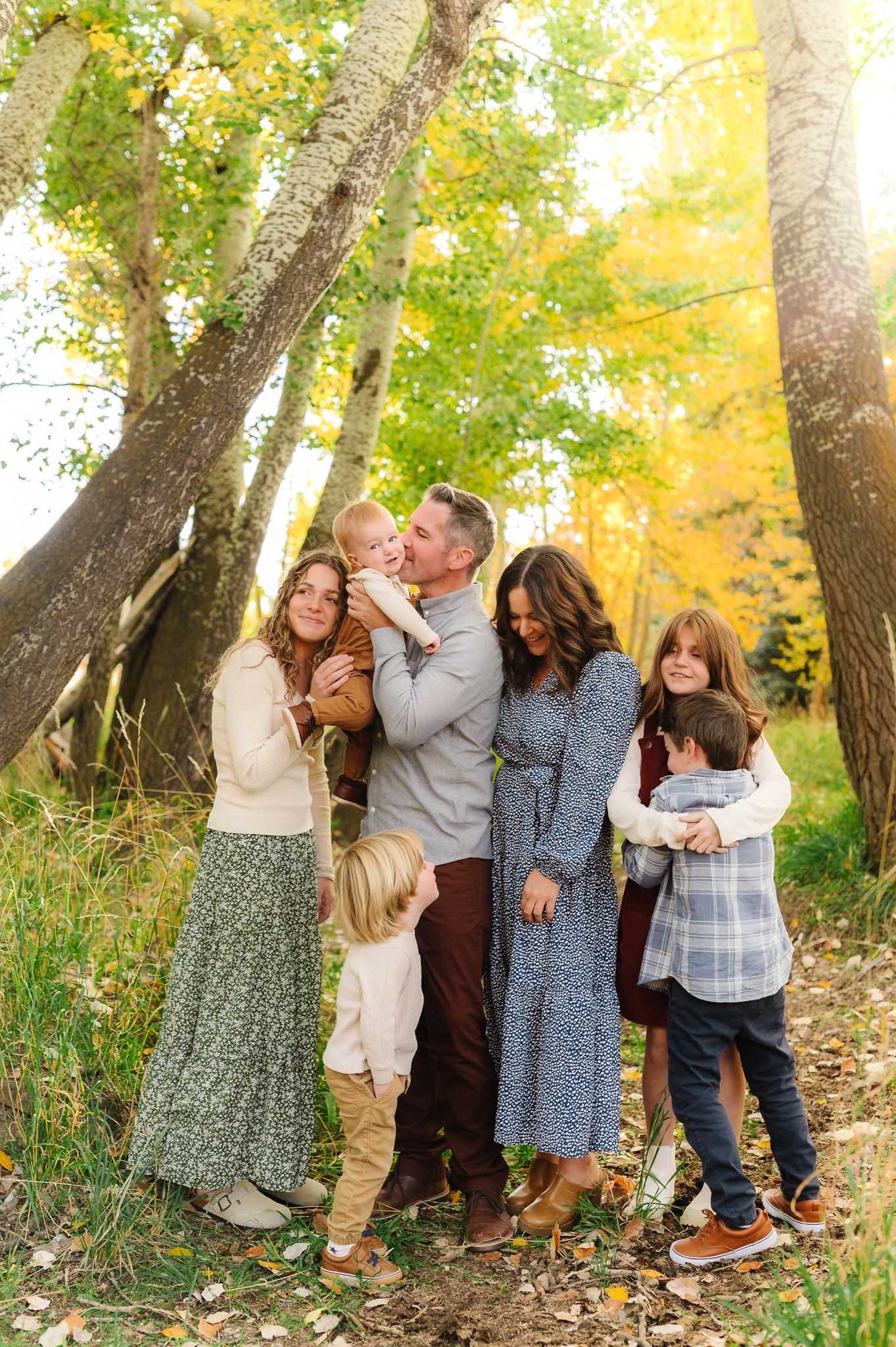 A group embraces while posing for a photo beneath fall trees with yellow foliage.
