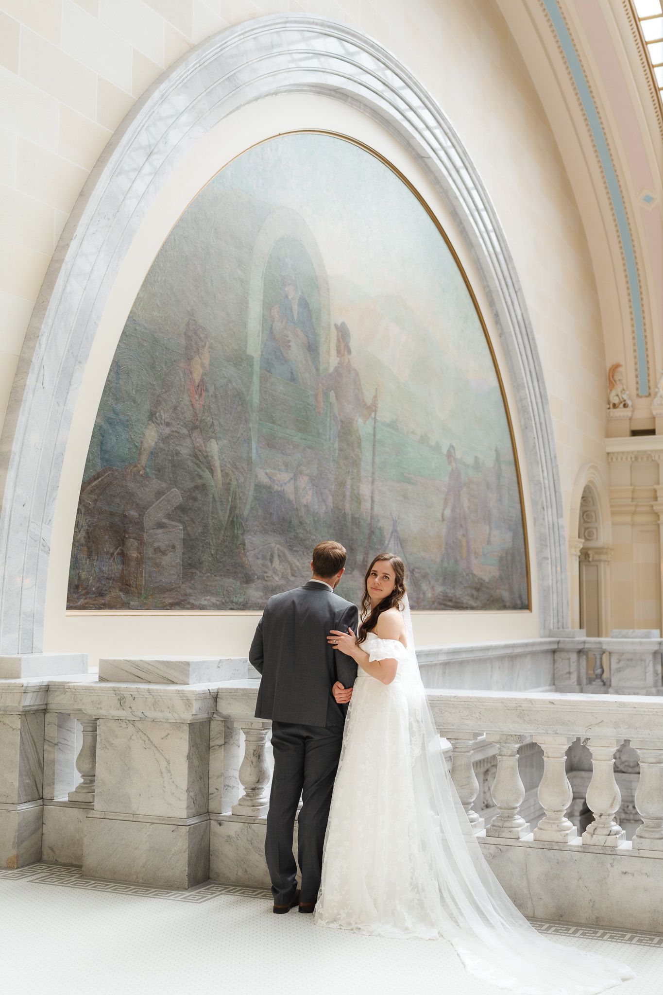 Wedding couple poses under arched hallway with painted murals and classical architecture.