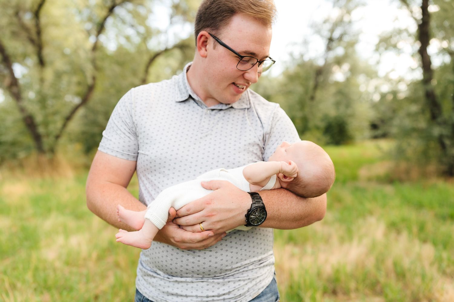 A gentle moment with a newborn baby being cradled outdoors in soft sunlight.