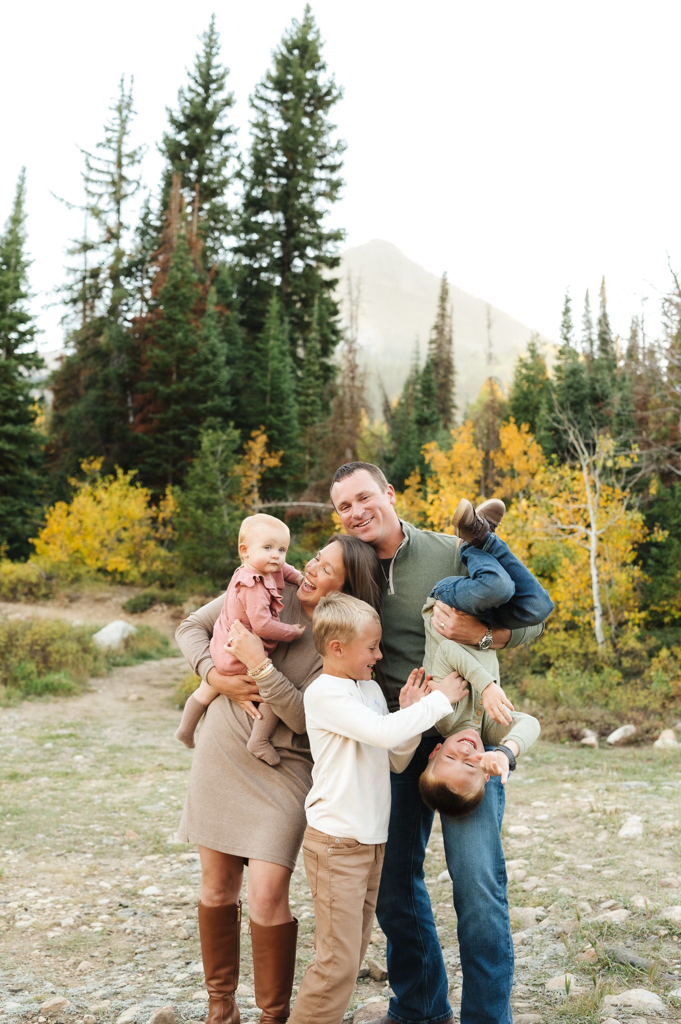 Family playing and embracing together in a mountain setting with yellow fall foliage and evergreen trees.