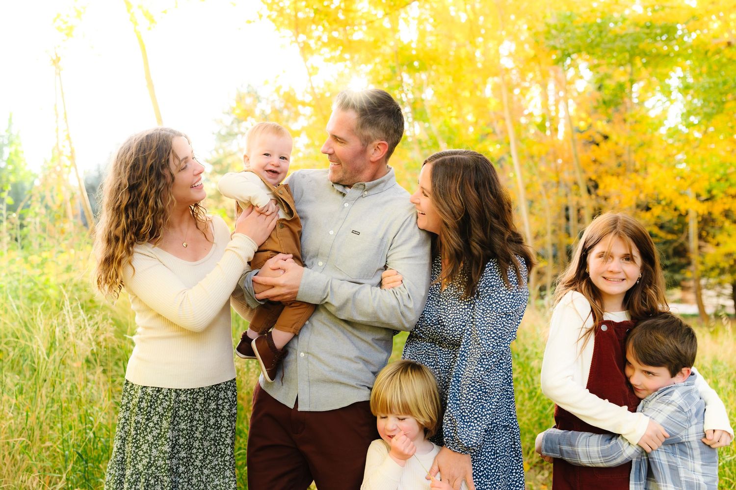 Natural light family photography session with everyone interacting playfully in an autumn forest.