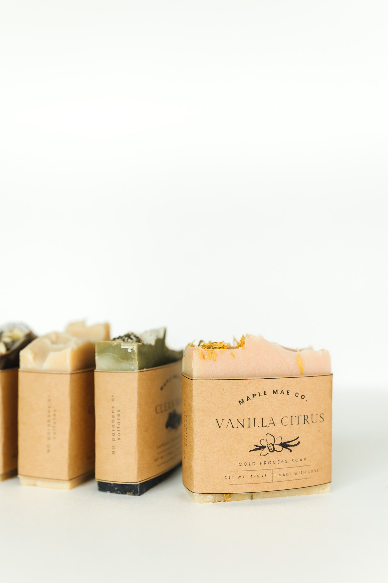 Row of natural soap bars in kraft paper packaging with minimalist branding and vanilla citrus scent label.