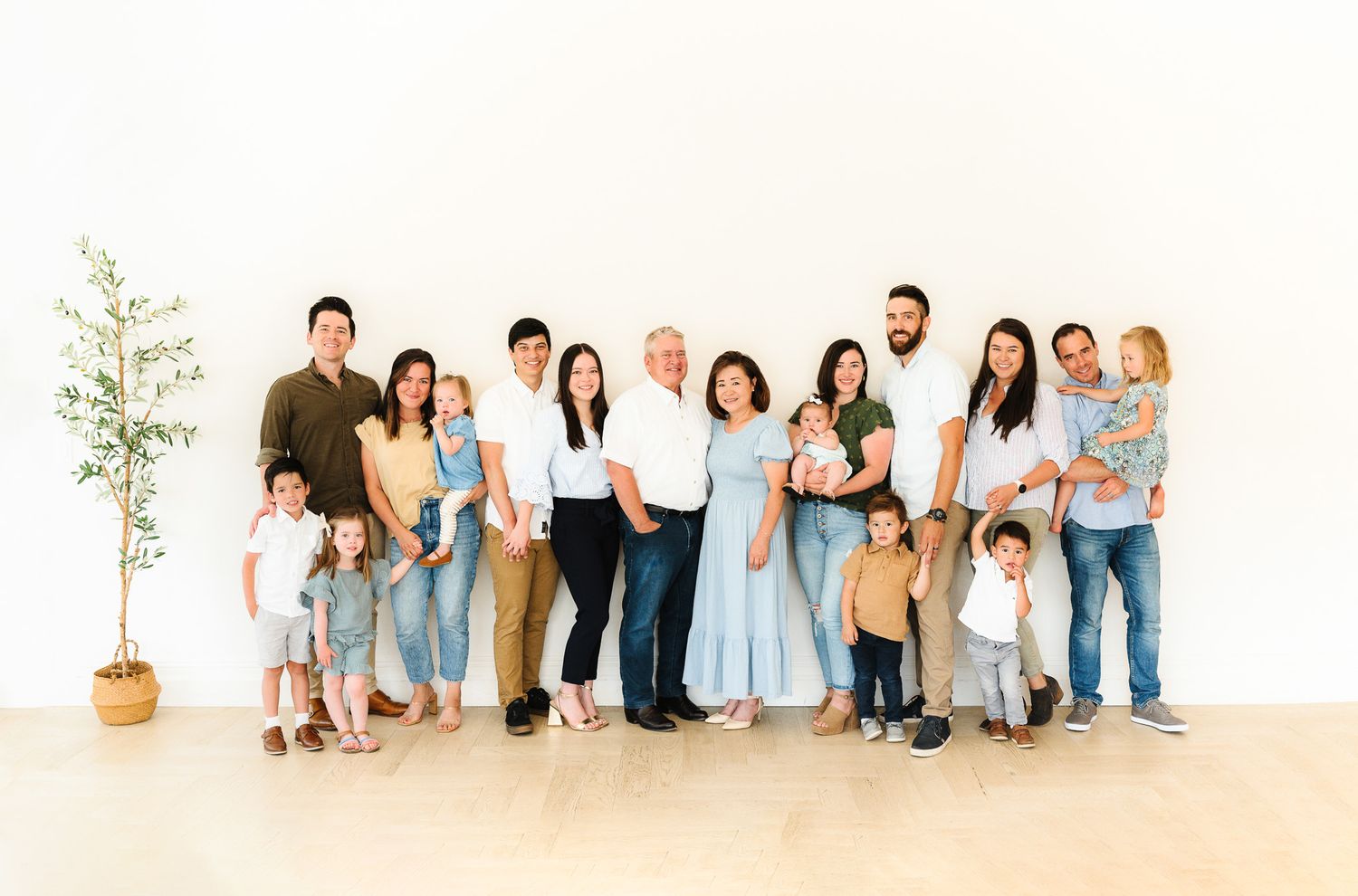 Extended family portrait session in a bright indoor studio with white backdrop and coordinated outfits.