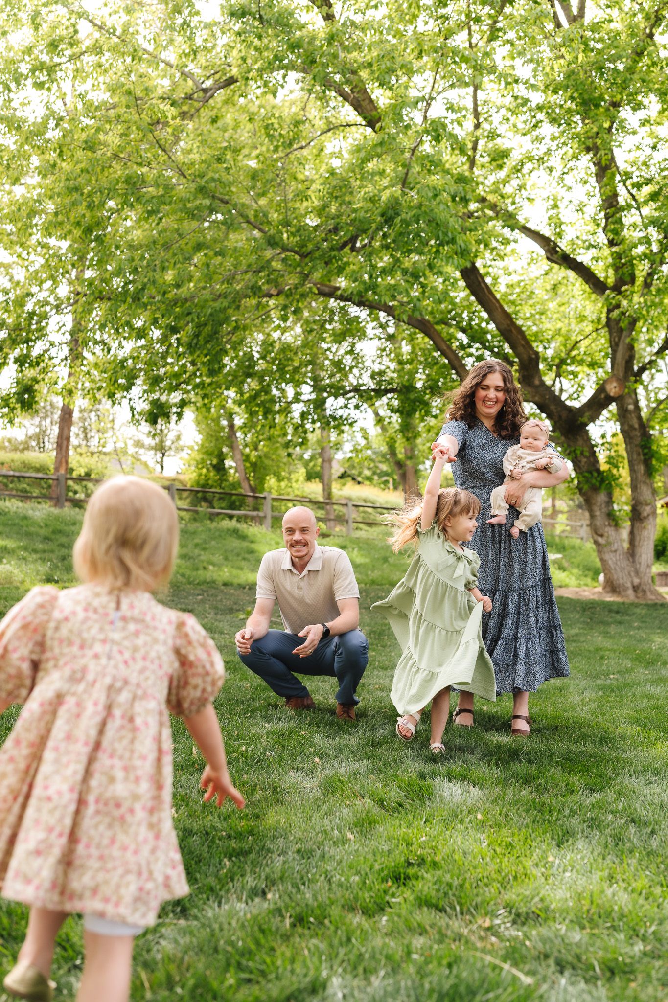 Happy family with two young girls and a baby enjoying a sunny day outdoors in a lush green park setting.