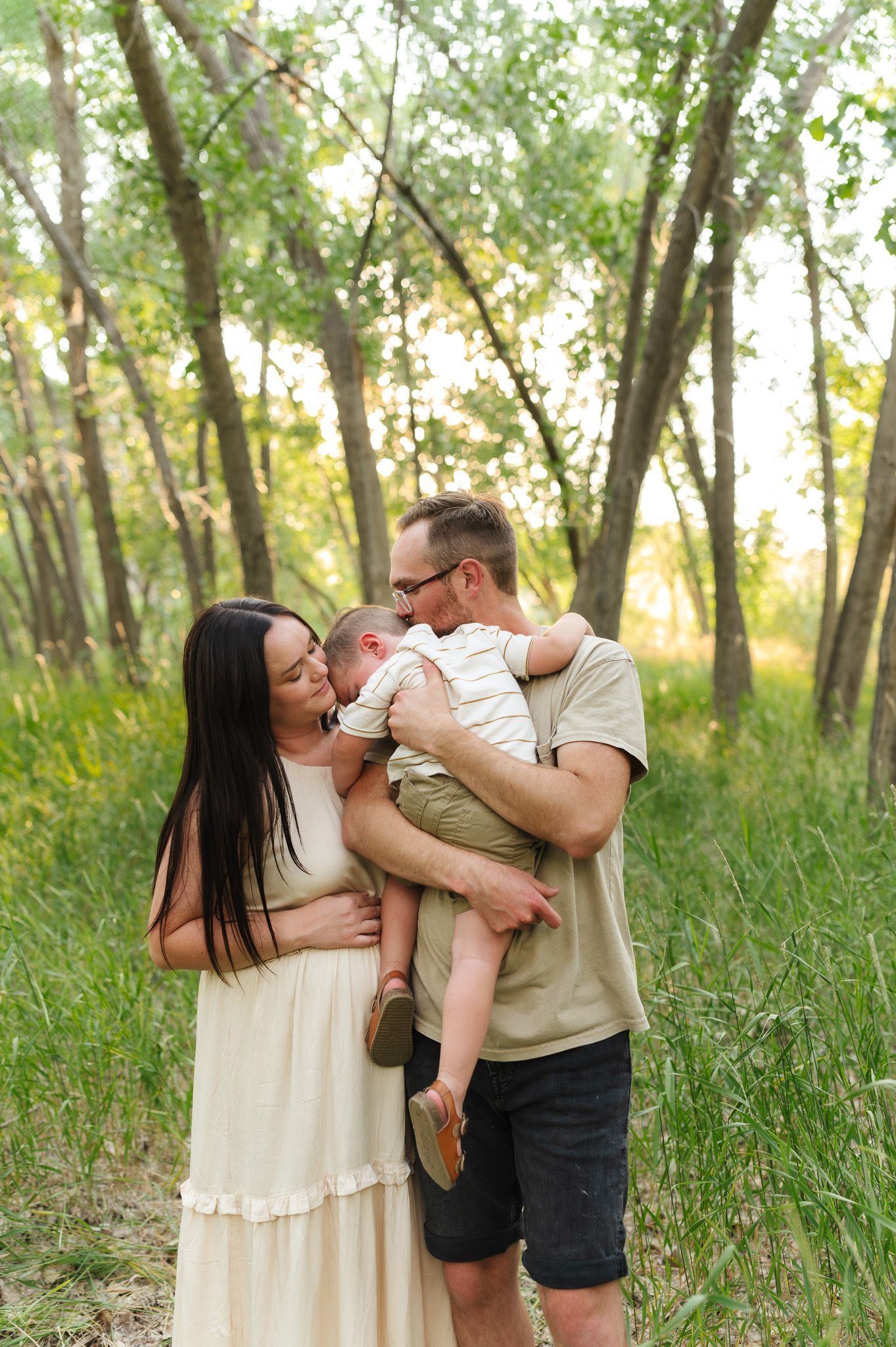 A couple stands in a lush green forest, lovingly holding their newborn baby during an outdoor family photo session.