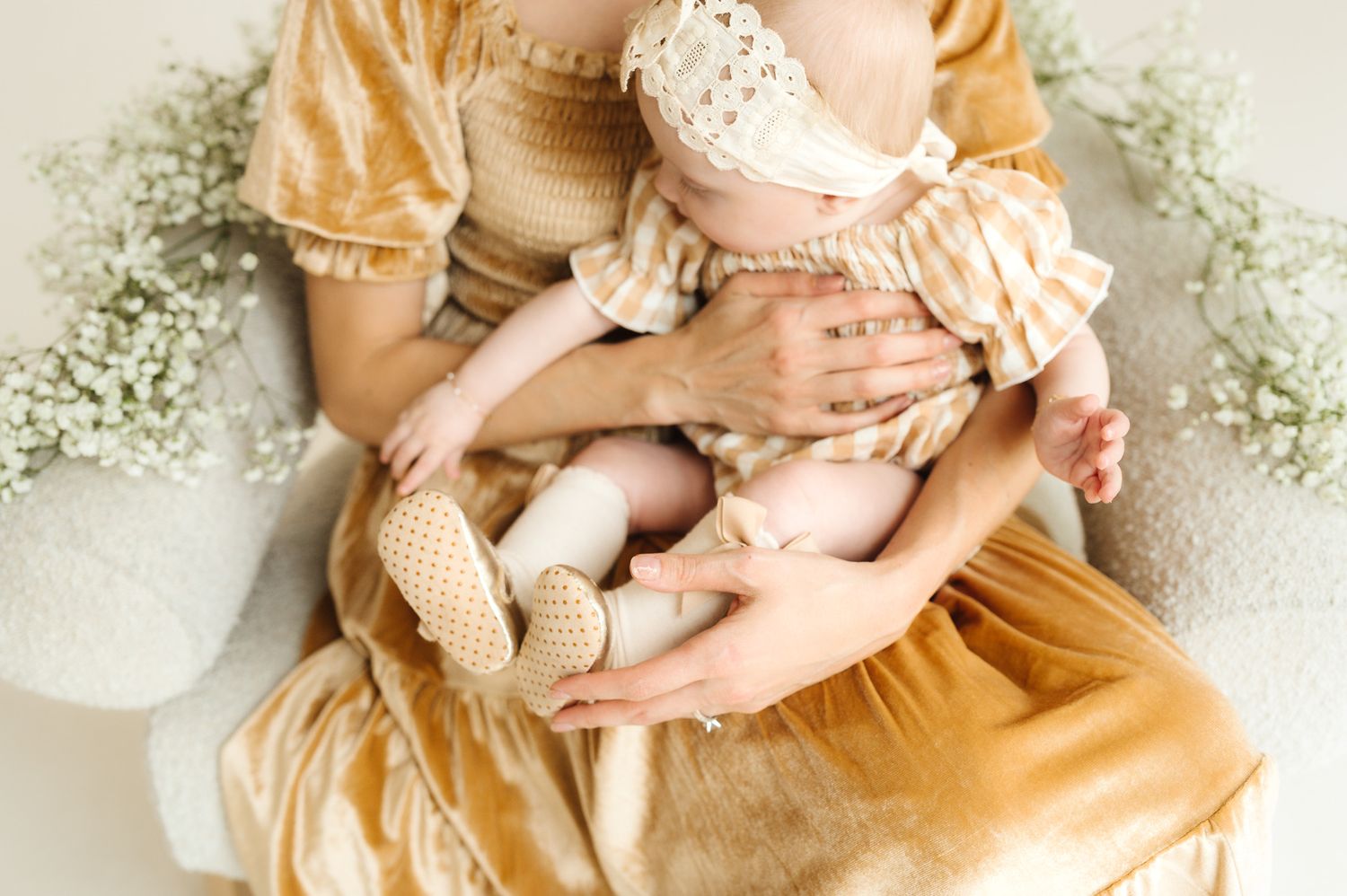 Mother in yellow vintage dress holding baby surrounded by baby's breath flowers.