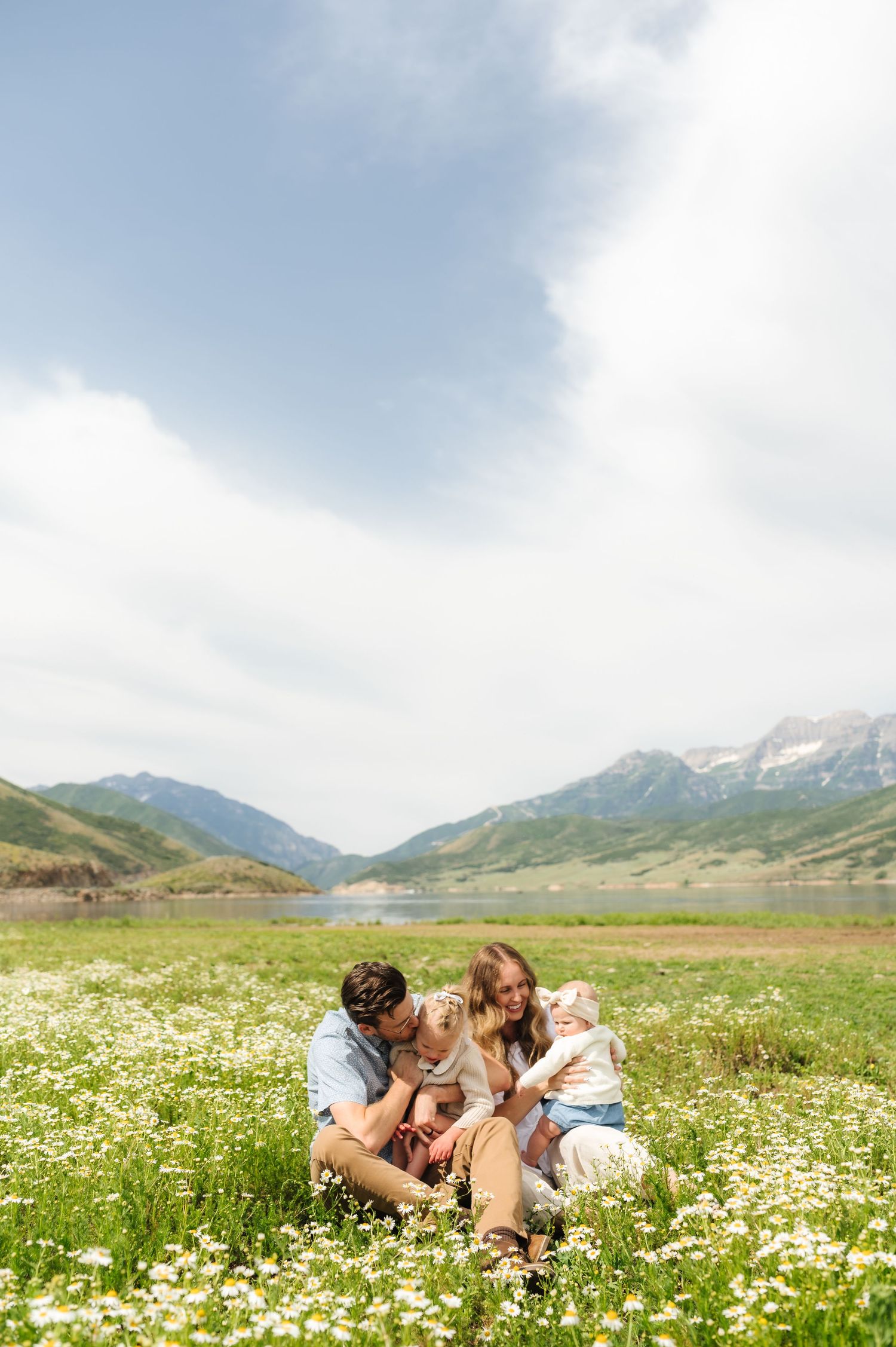 A couple lies together in a scenic mountain meadow filled with blooming white wildflowers on a sunny summer day.