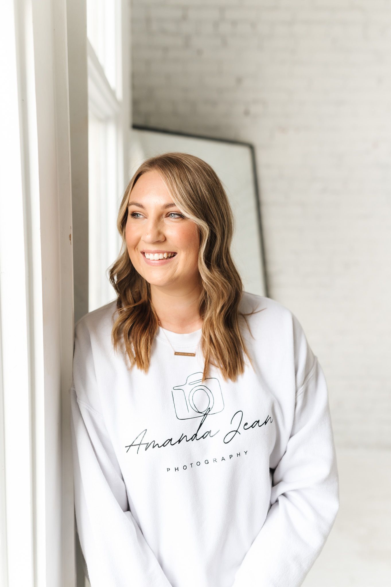 Photographer in white branded sweatshirt standing by window in bright studio space.