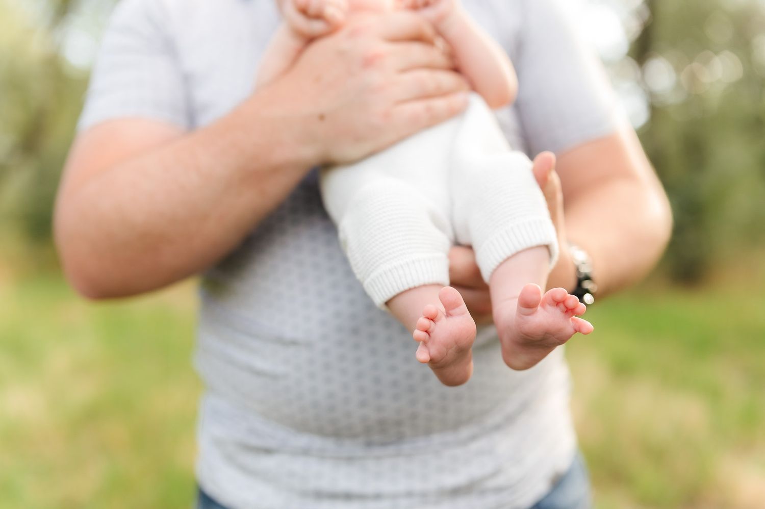 Tiny baby feet being held gently against a blurred natural outdoor background.